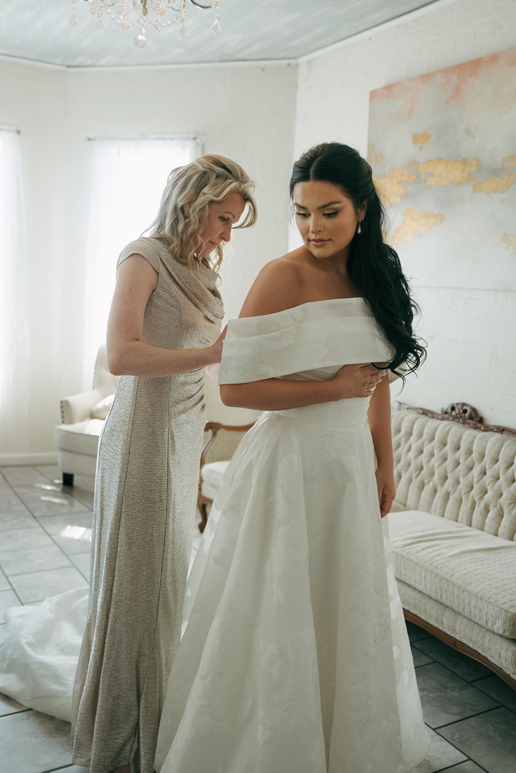 Mom helps the bride into her long gown in the getting ready room