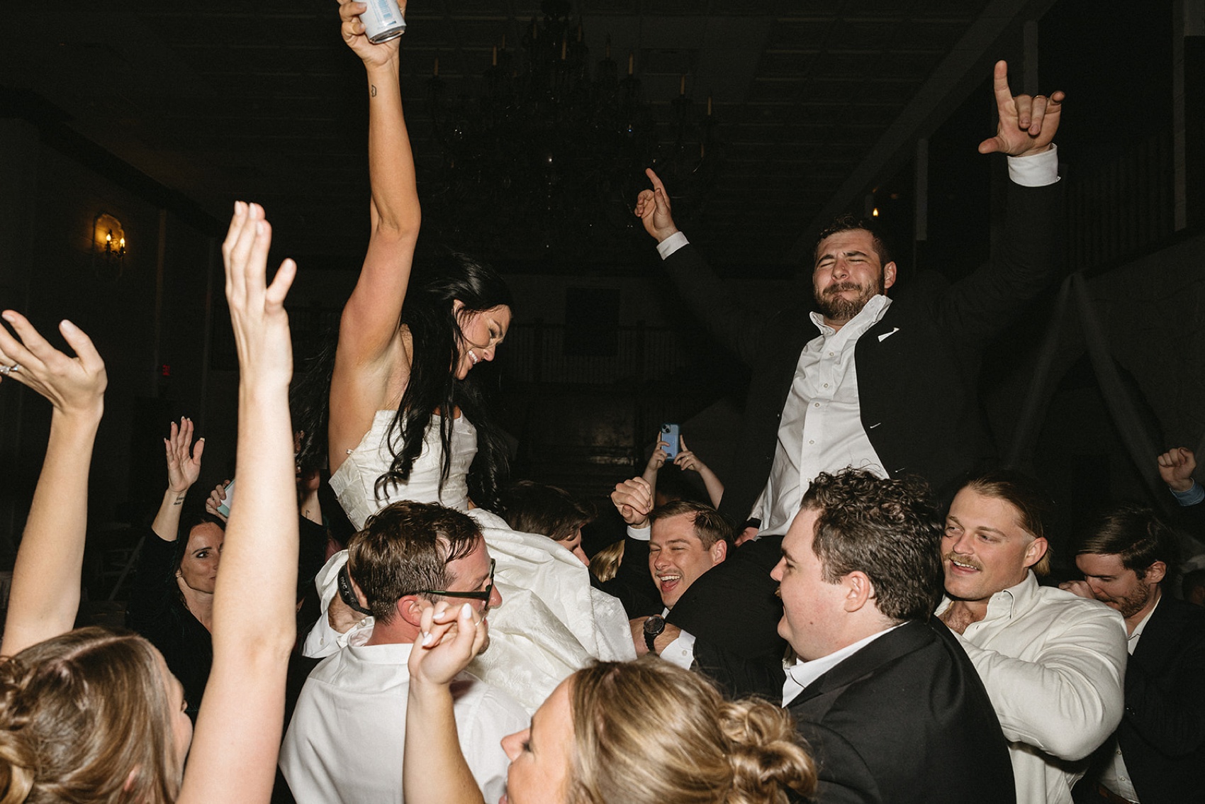 A bride and groom are lifted on the wild dance floor with hands in the air