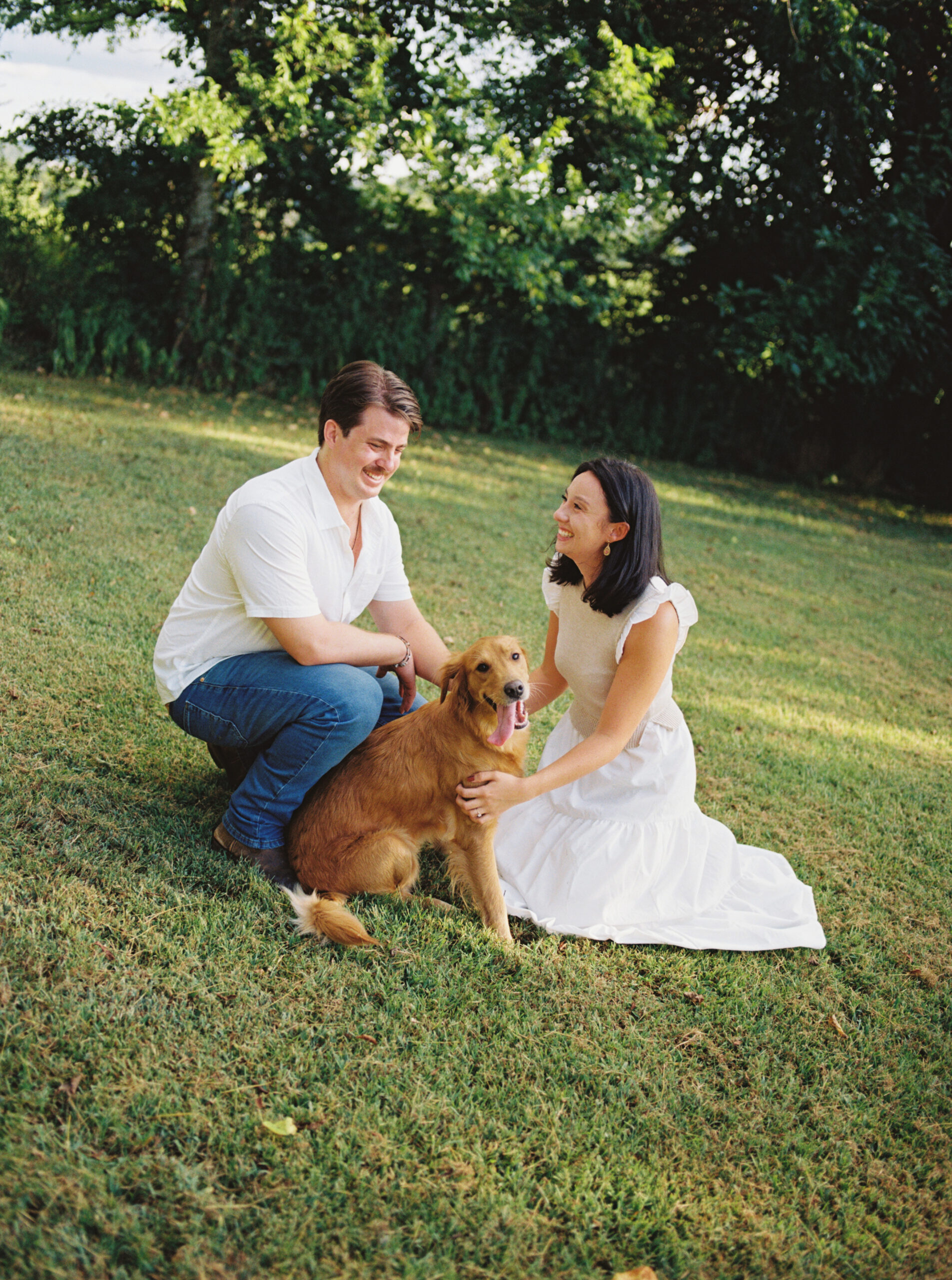 Couple petting their golden retriever laughing at each other wearing white.