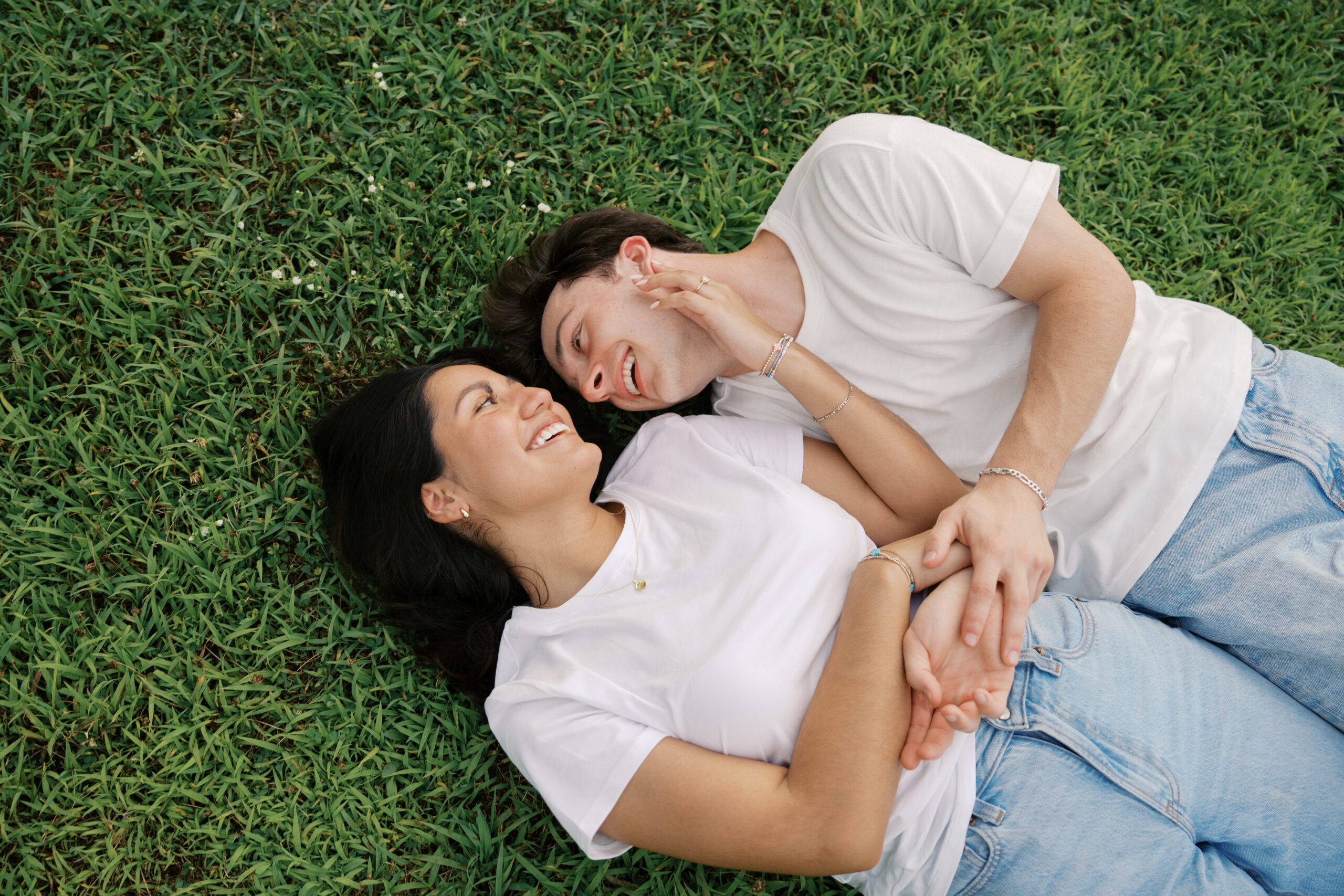 Couple holding each other laughing in a field surrounded by flowers in white t-shirts and blue jeans in Nashville, TN.