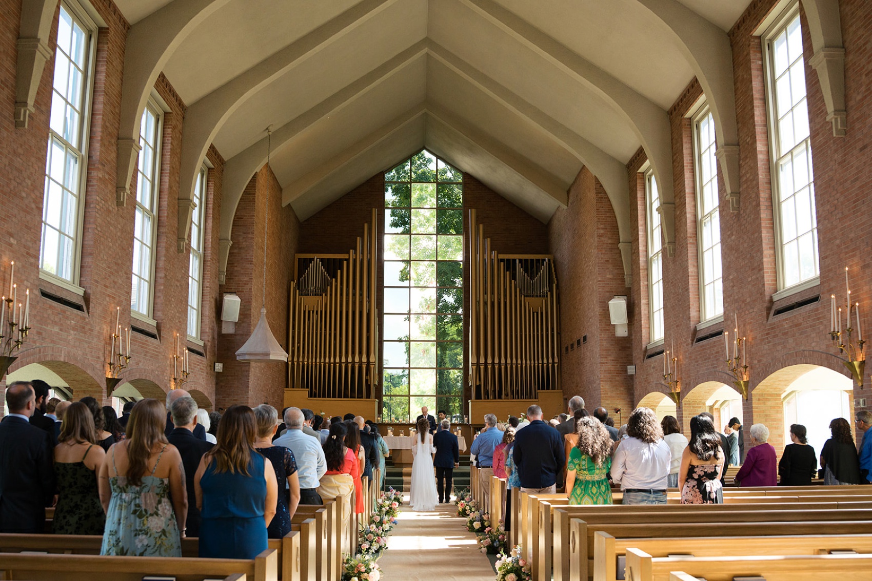 A look down the aisle of a bride standing at the altar with dad walking her as guests stand watching