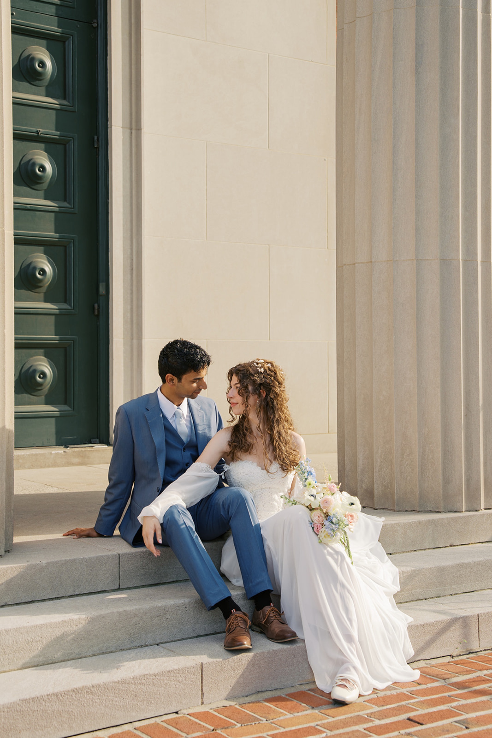 A bride leans on her groom in a blue suit on the steps of the vine street christian church wedding venue