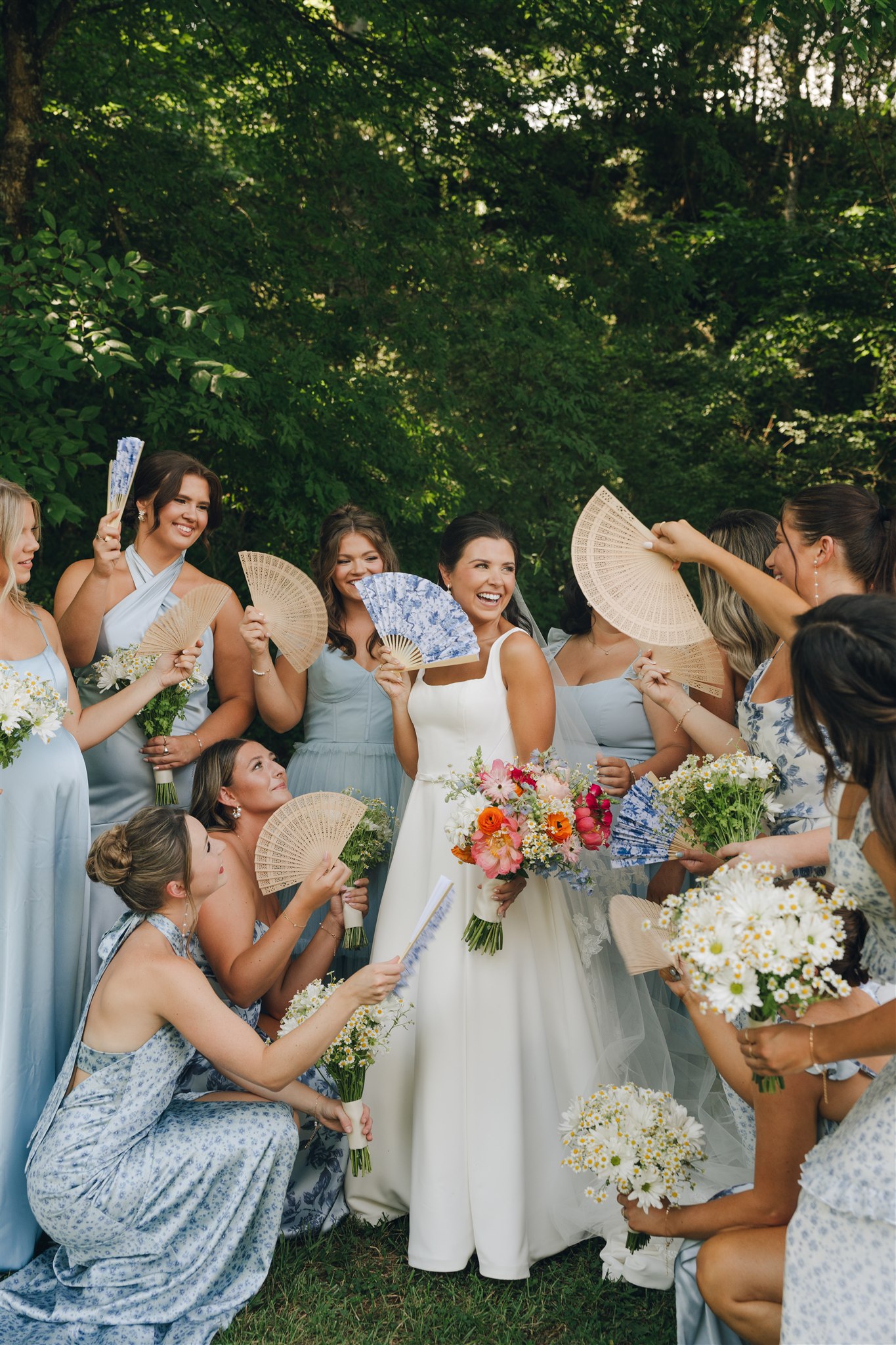 A bride laughs while being fanned by her bridesmaids in blue