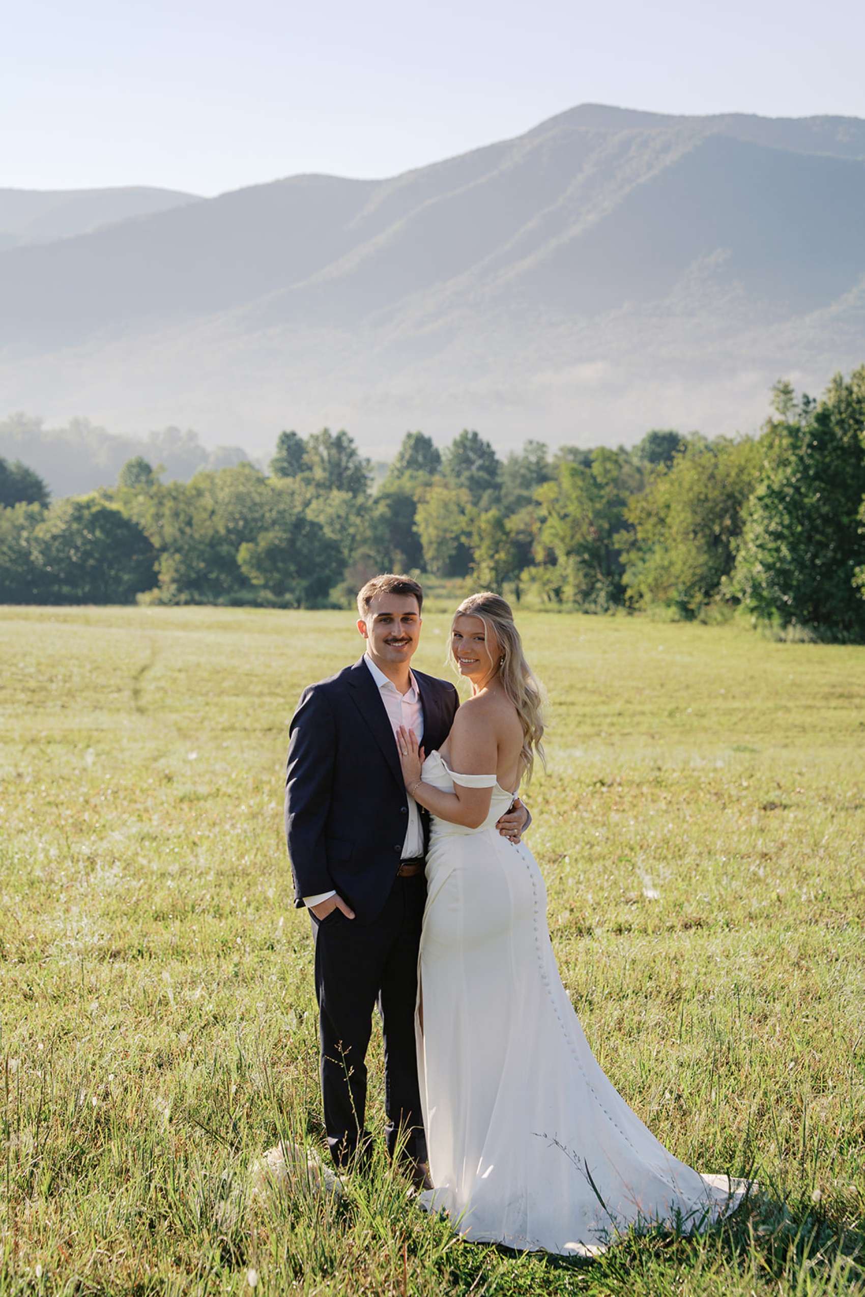 Newlyweds stand smiling while cuddling in a large meadow during their cades cove wedding