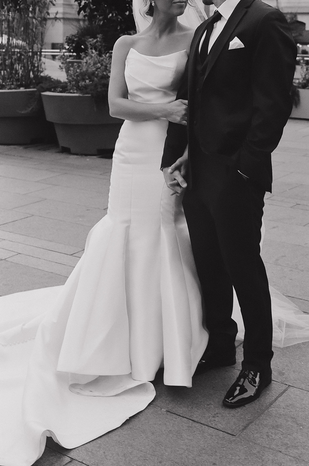 Newlyweds stand in downtown sidewalk holding hands and smiling at each other