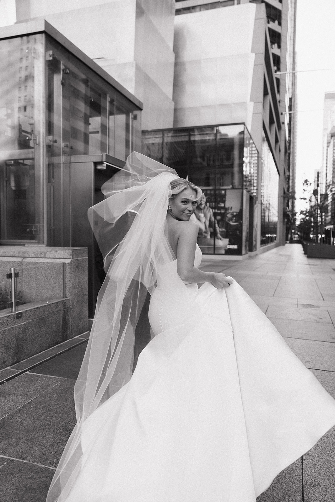 A bride smiles over her shoulder while walking downtown holding her train to her The Hermitage Hotel wedding