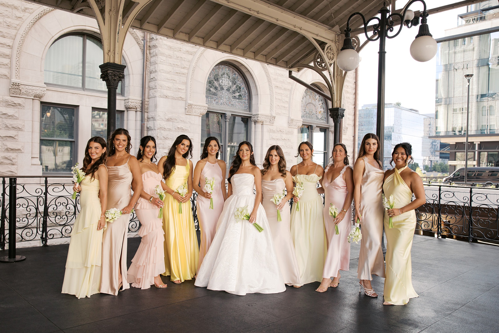 A bride stands holding her bouquet with her bridesmaids in white and yellow at her union station wedding in nashville