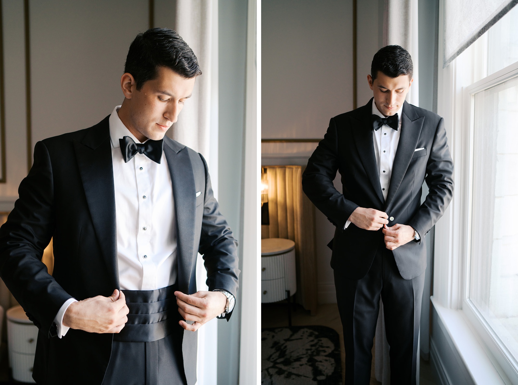 A groom buttons his jacket while standing in a window in his black tuxedo