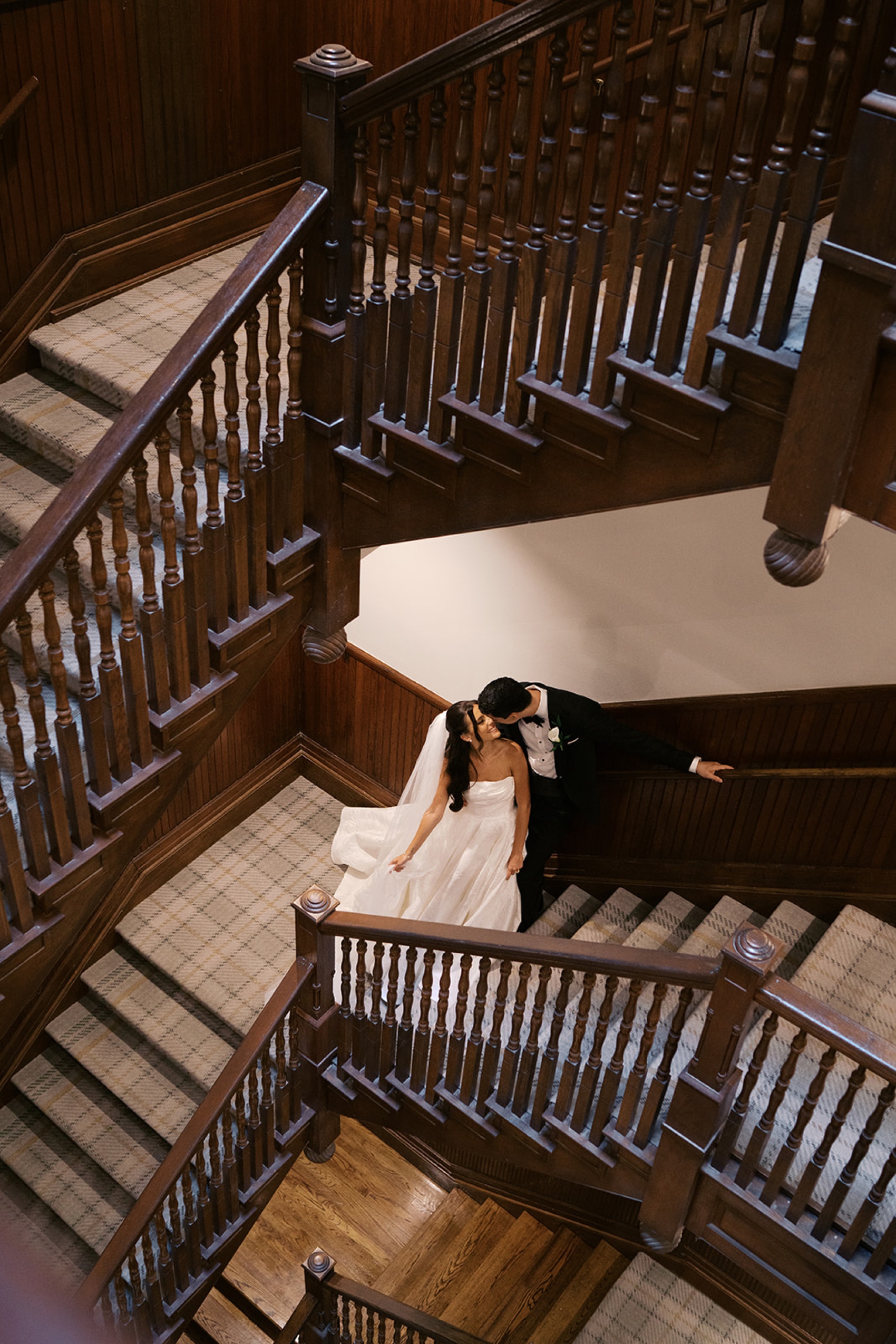 A look down the grand wooden staircase as newlyweds lean in for a kiss at their union station wedding in nashville