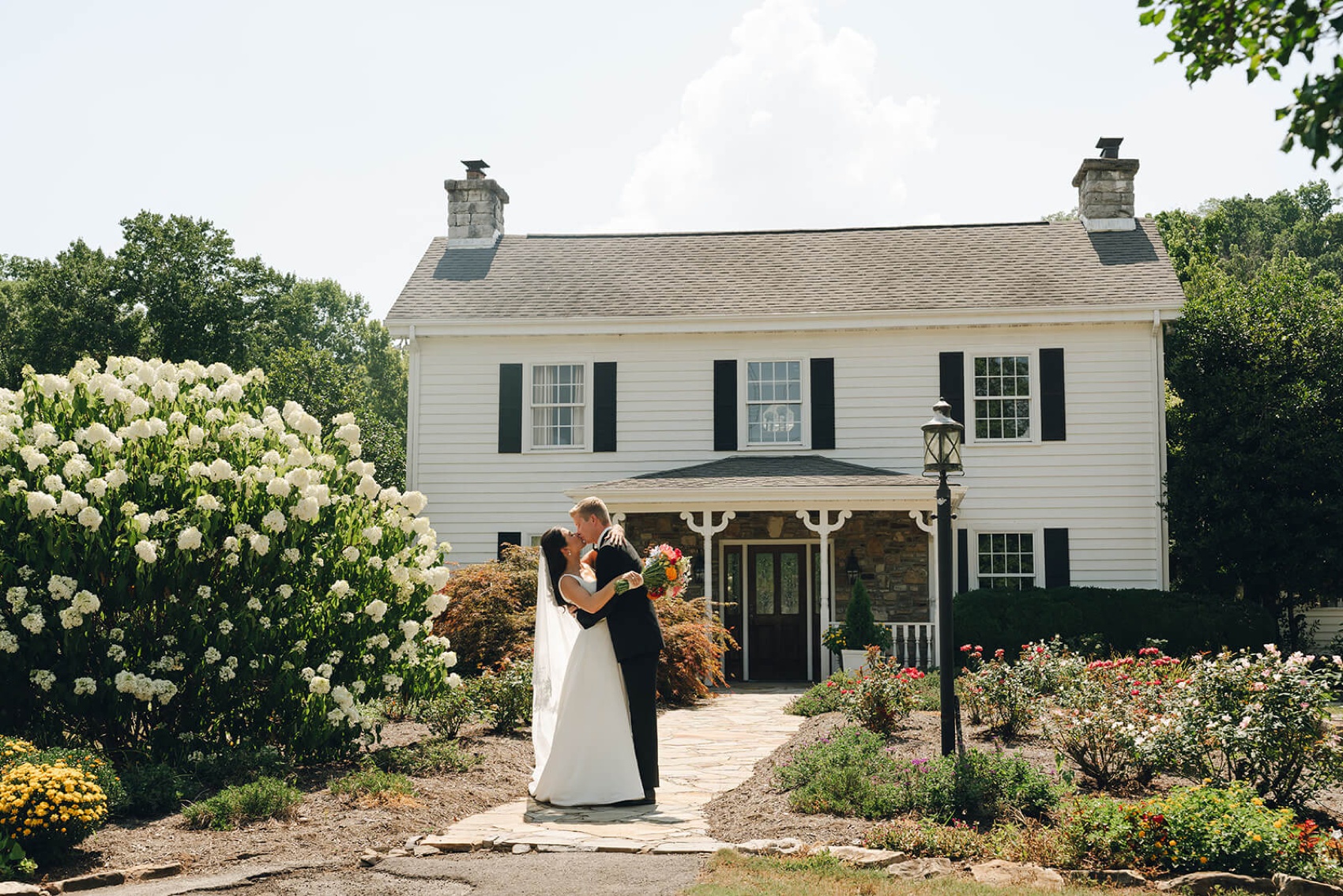 Newlyweds kiss in the stone garden path leading to a white building