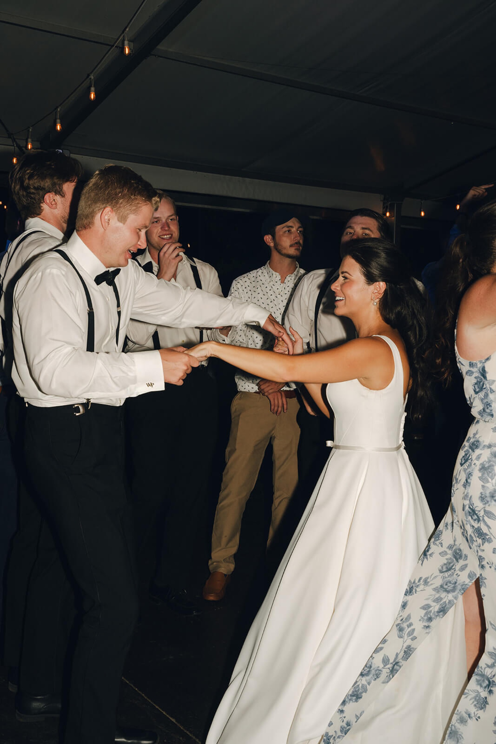 A bride and groom laugh and dance with guests on the dance floor