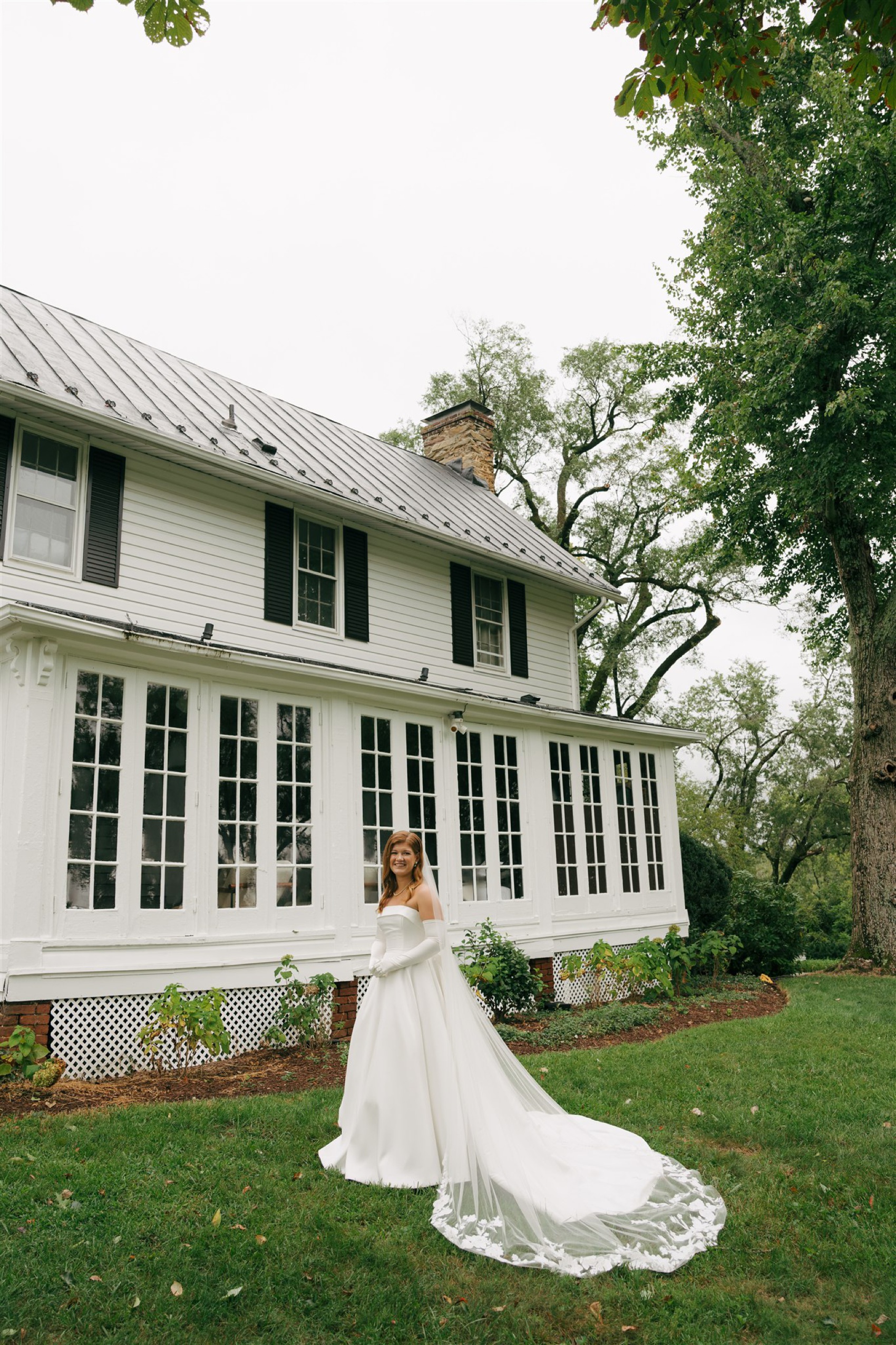 a bride smiles with her long embroidered veil spread behind her in the back lawn of Black Horse Manor