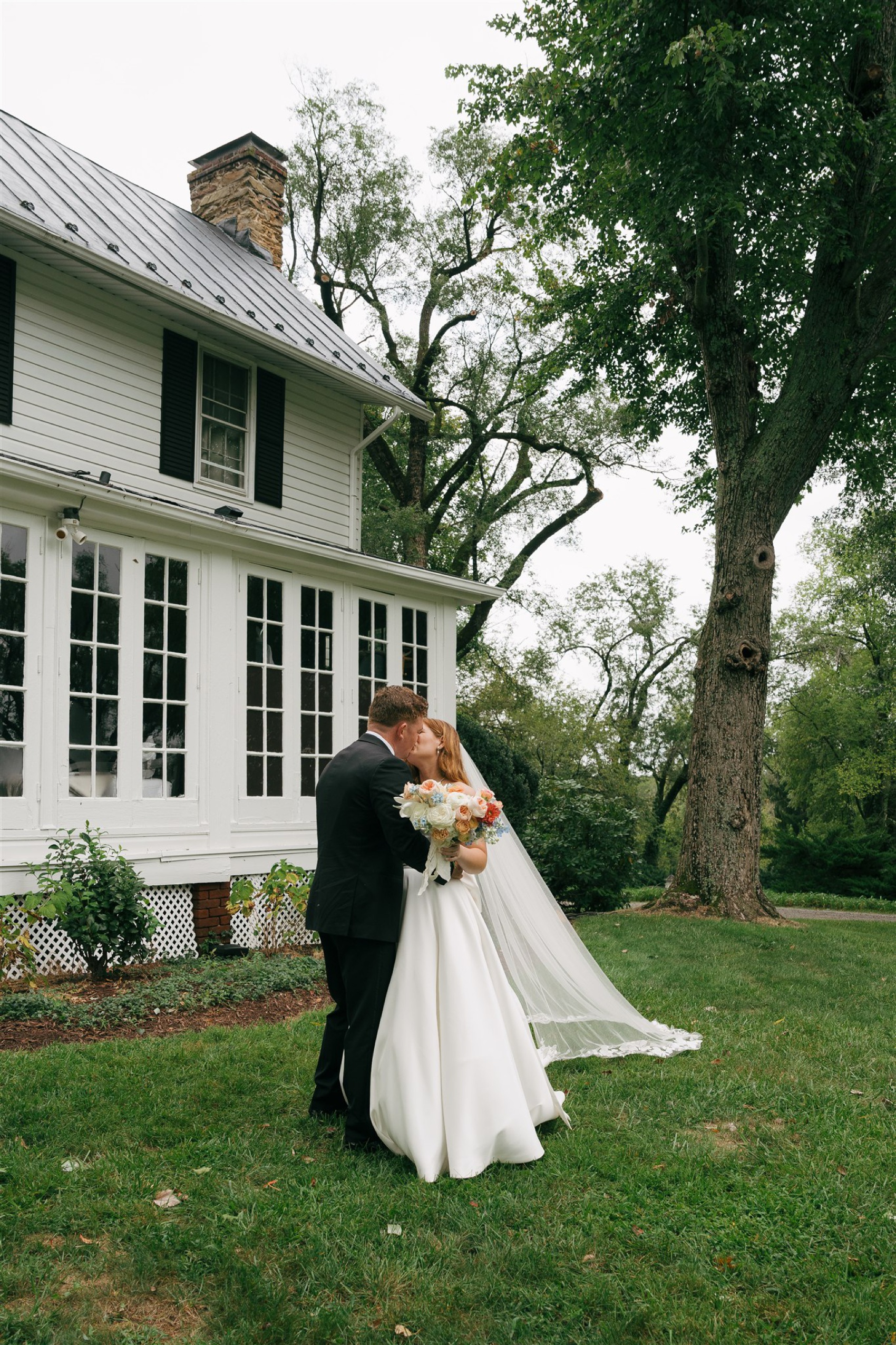 newlyweds kiss while in the lawn of the Black Horse Manor holding a large bouquet