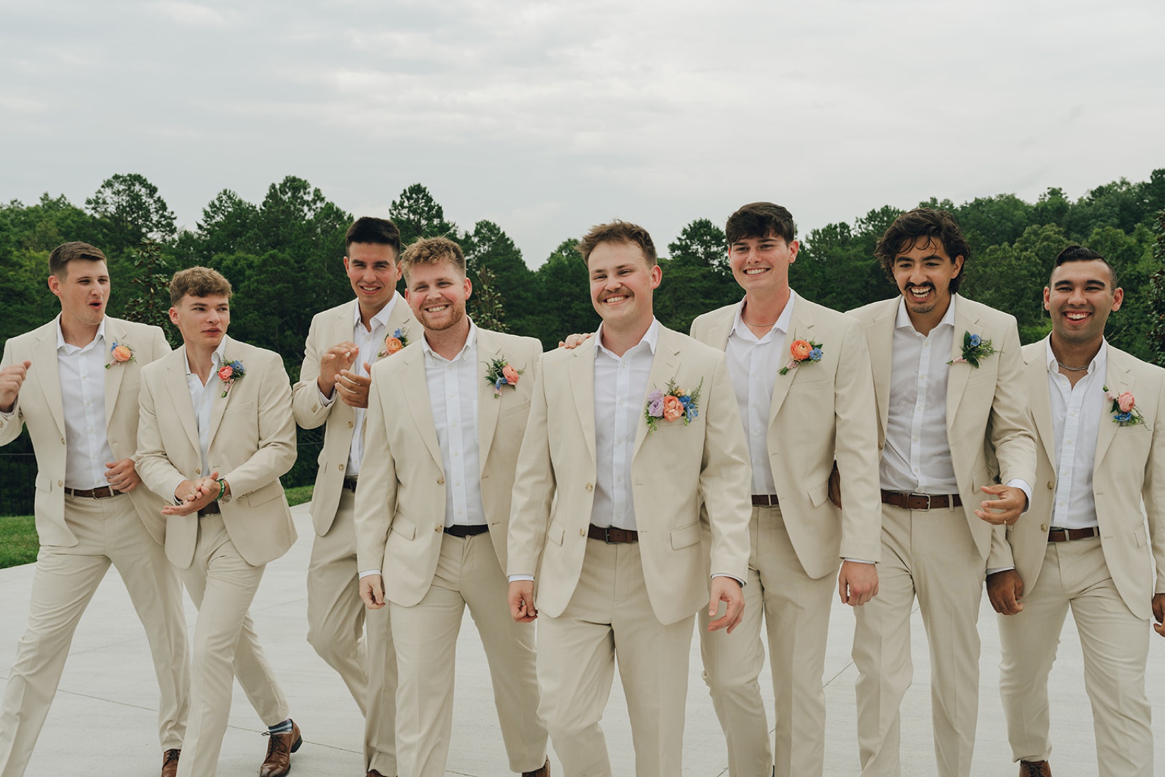 A groom smiles while walking a patio with his groomsmen in matching khaki suits
