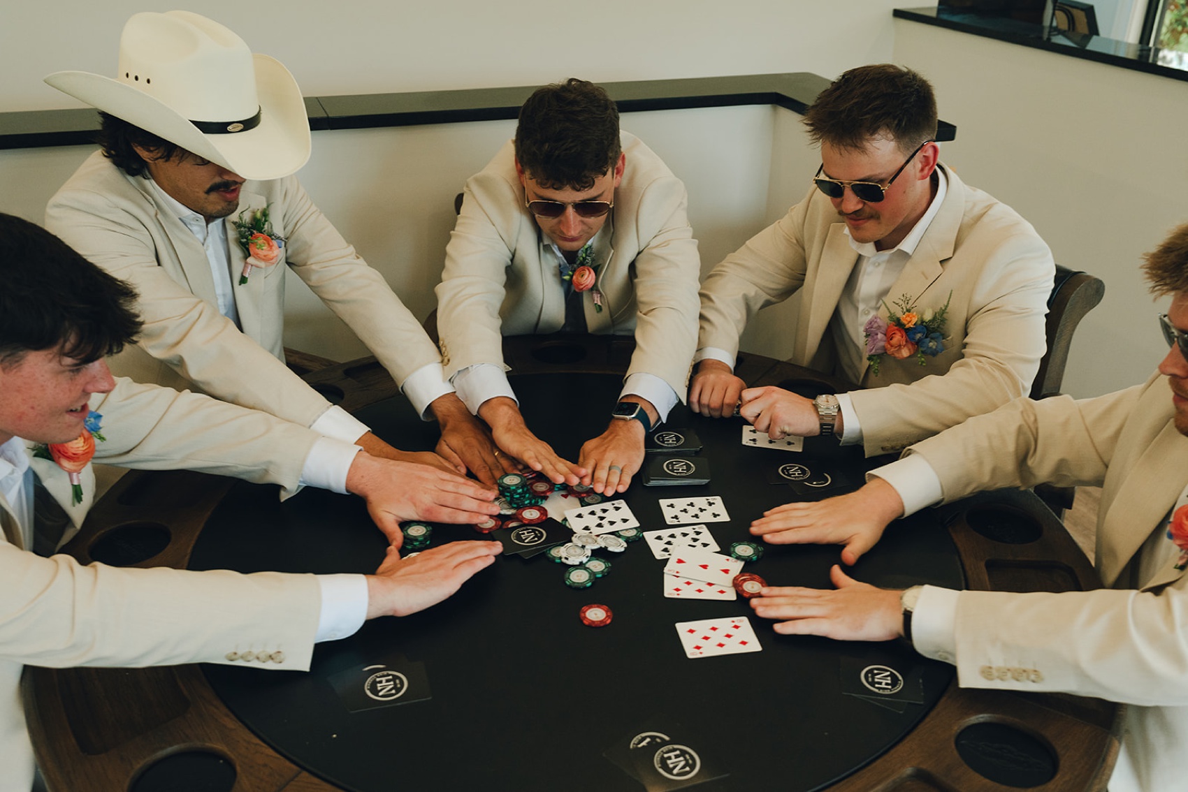 A groom pushes his chips all in with his groomsmen all in matching khaki suits and sunglasses at a poker table