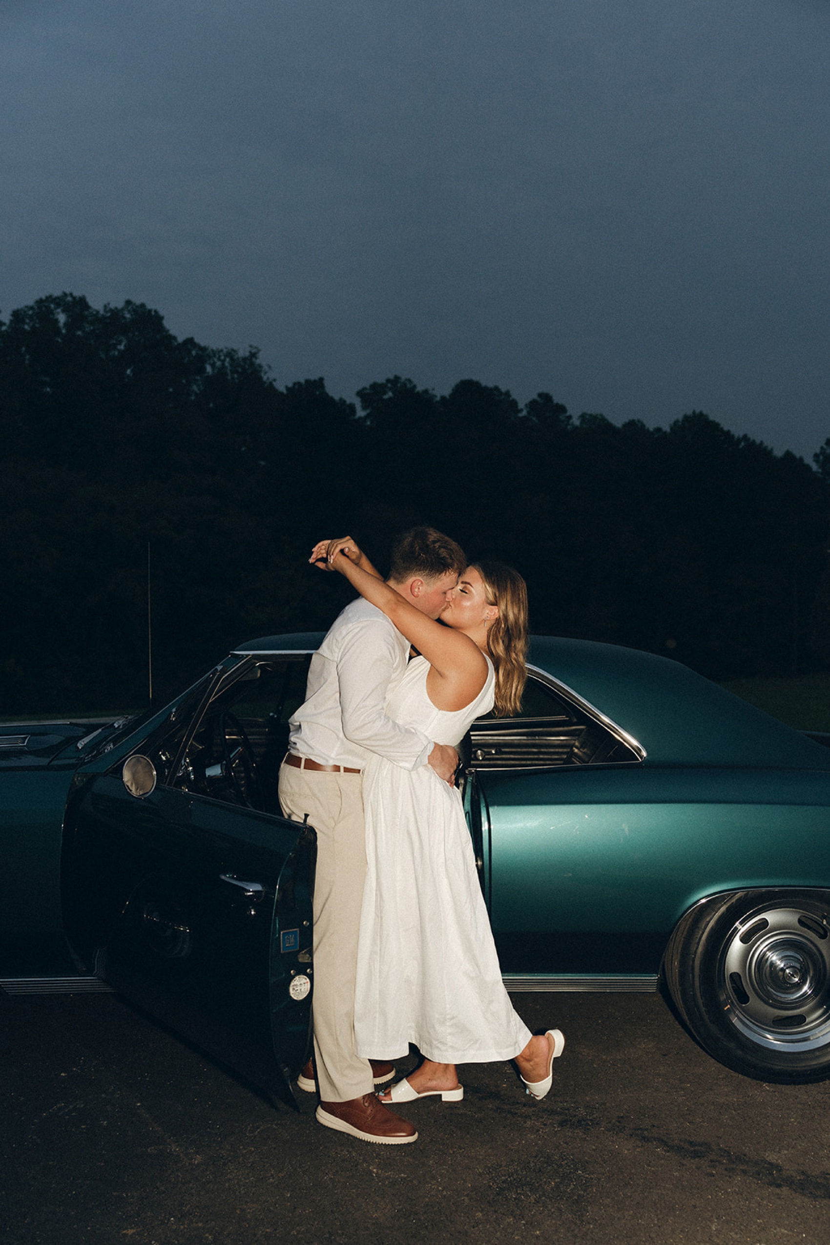 Newlyweds share a happy kiss while standing in the door of a vintage green muscle car