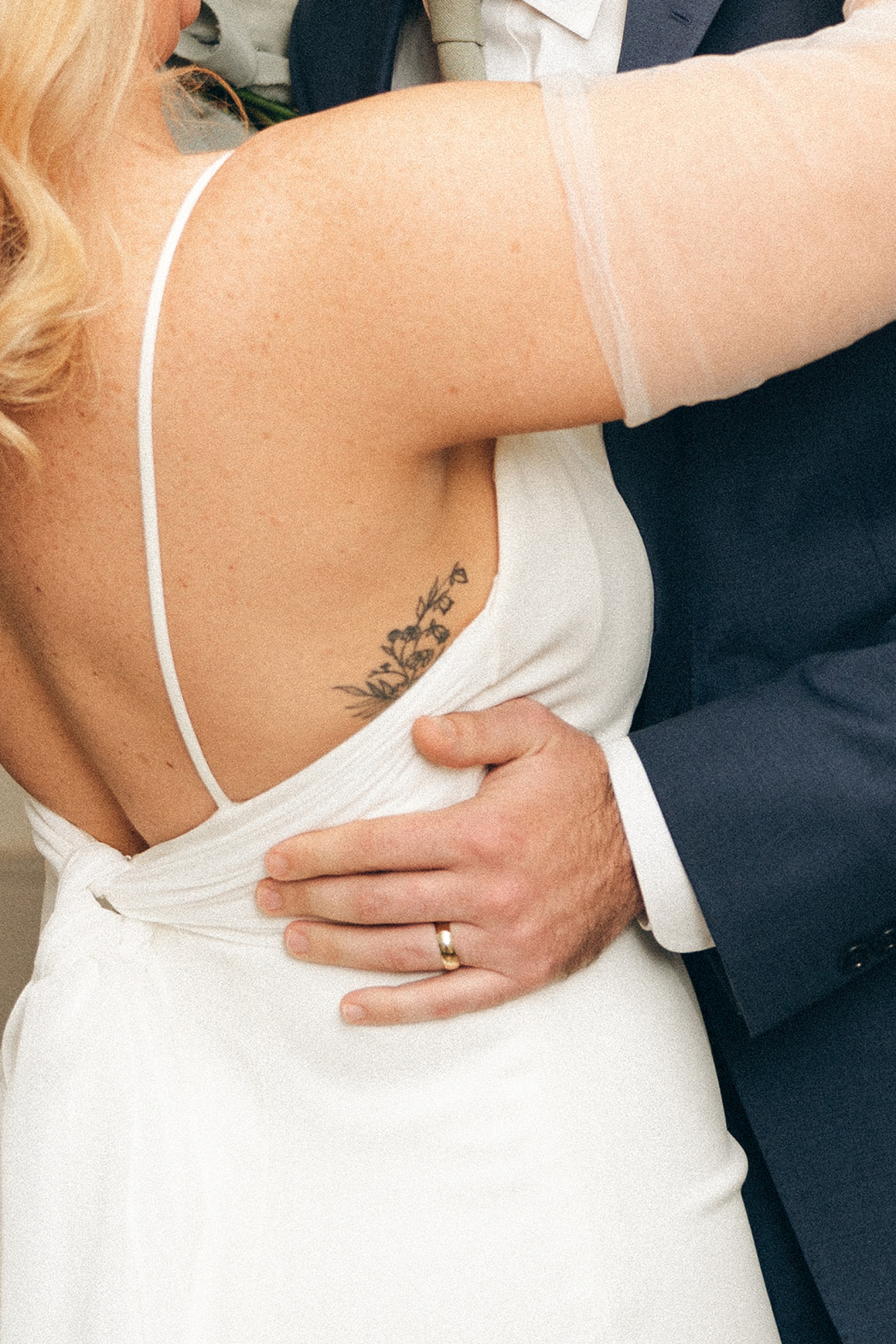 Details of a groom's hand on his bride's waist as they hug