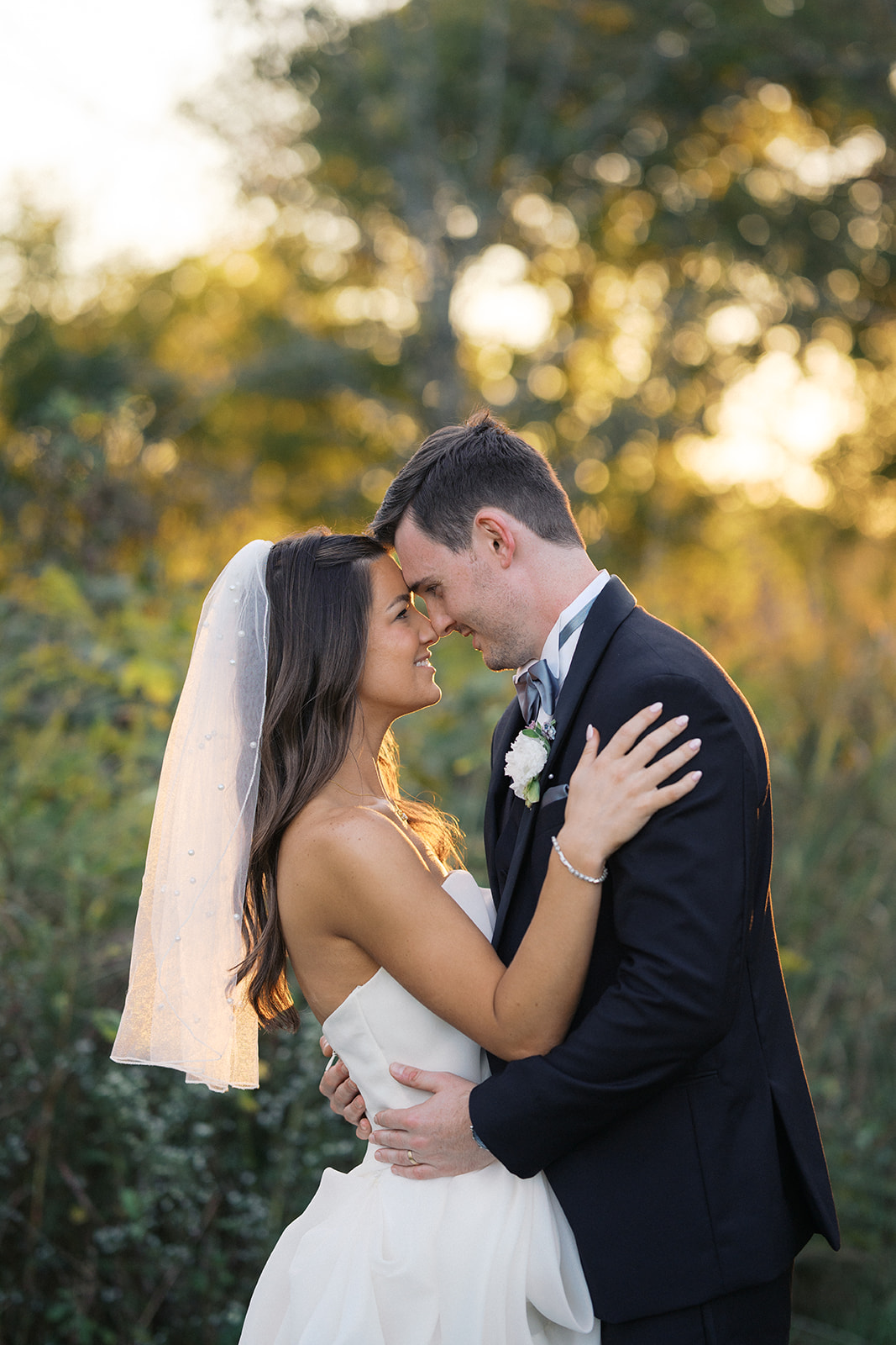 A bride and groom smile big while touching foreheads at sunset during their Crane Estate wedding