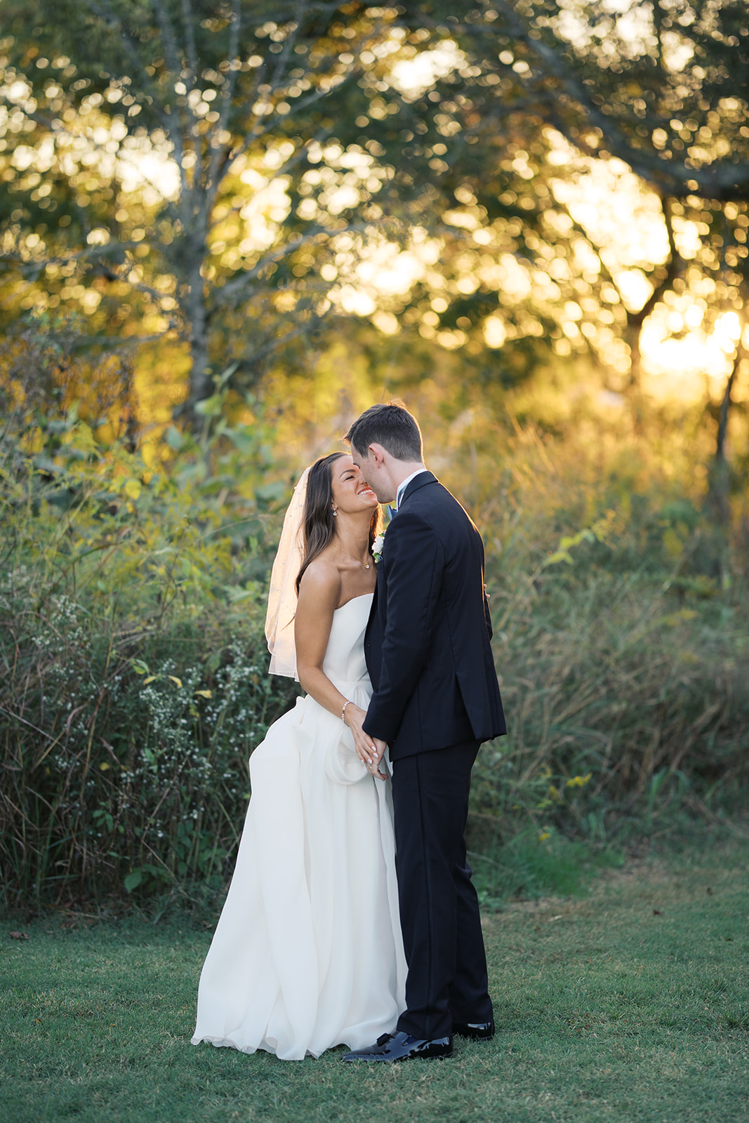 newlyweds share a happy kiss while holding hands in a garden at sunset during their Crane Estate wedding