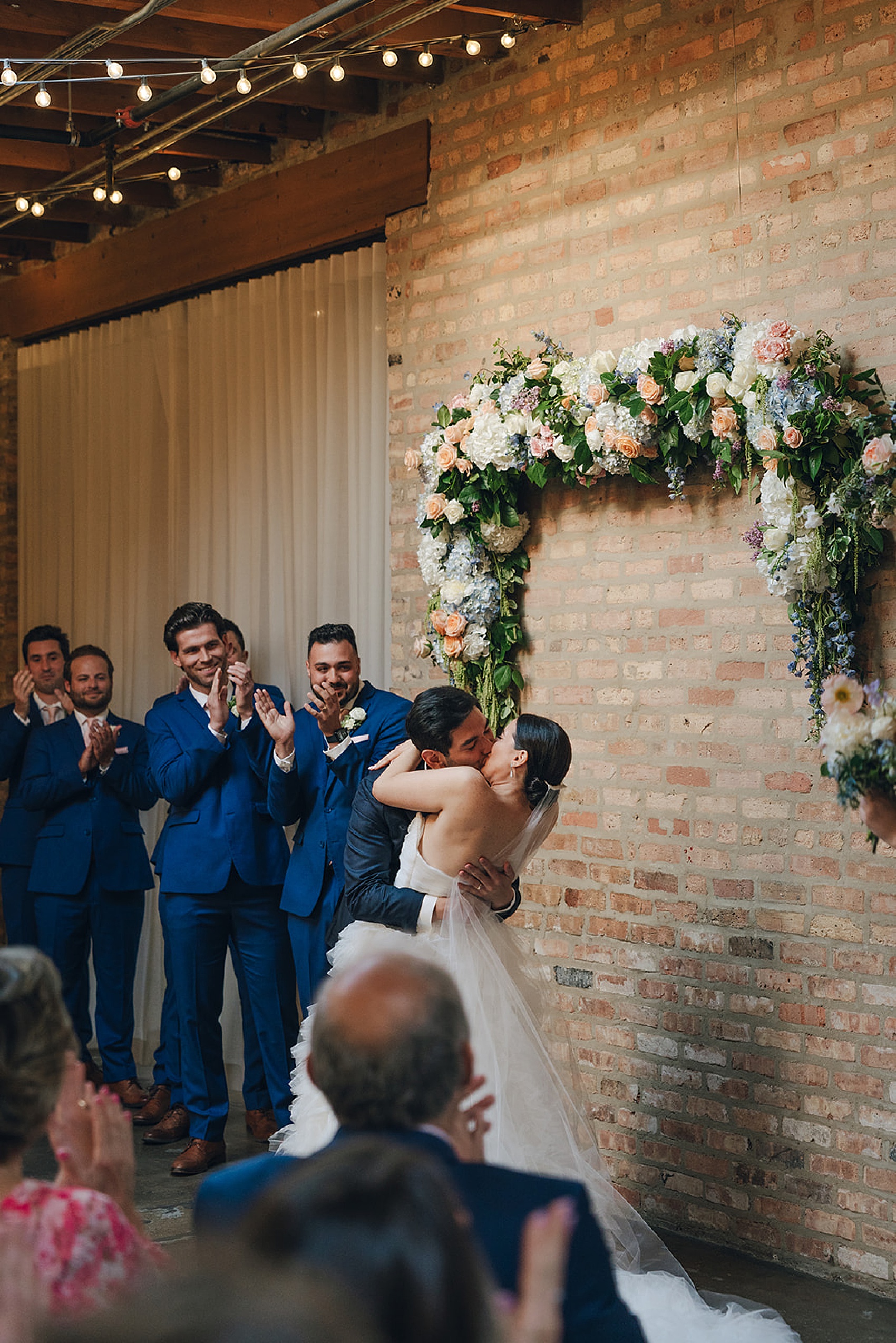 Newlyweds kiss to end their ceremony under a wall mounted floral arch at The Arbory
