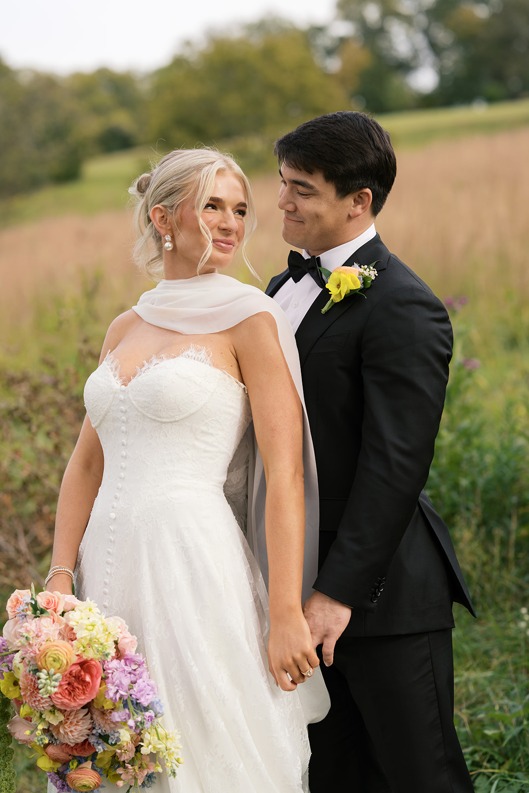 A bride leans in the chest of her groom while smiling up to him in a meadow during their Blackberry Farm wedding
