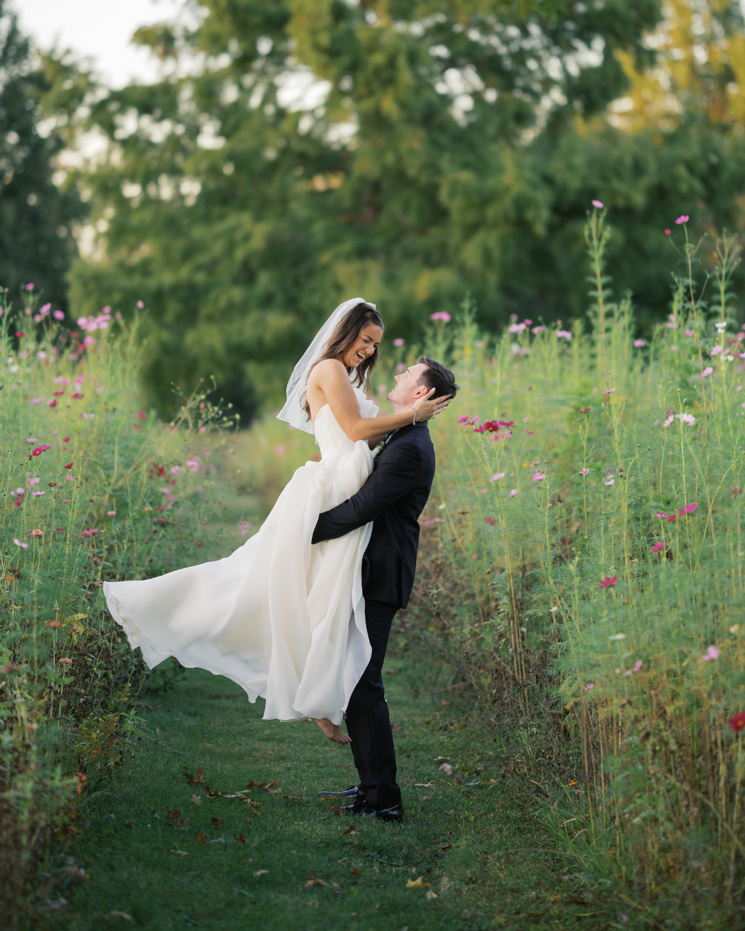 a bride and groom smiling and laughing in a field full of pink and purple wildflowers at long hollow gardens in gallatin tennessee