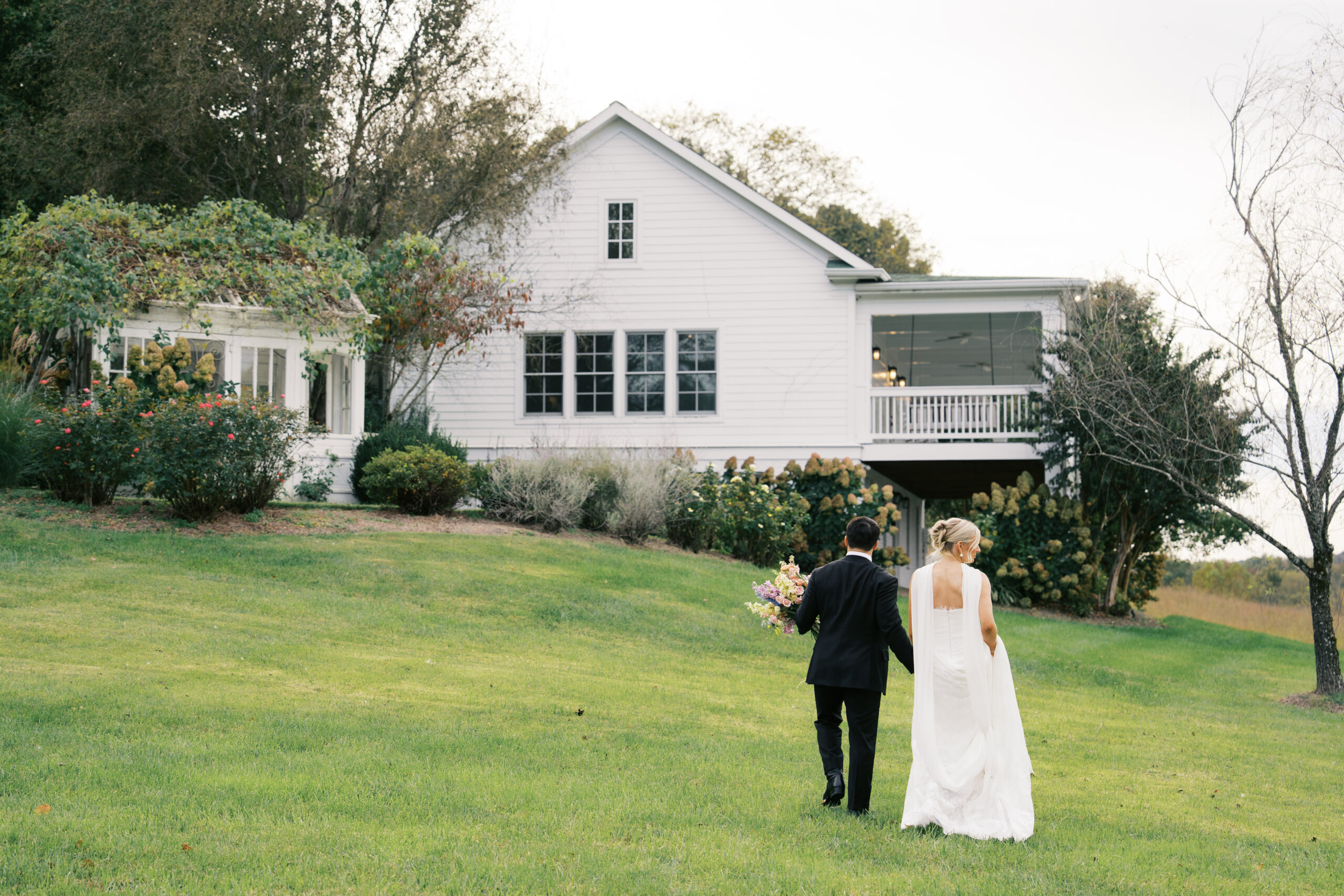 A bride and groom are holding hands while walking in a field at mint springs farm