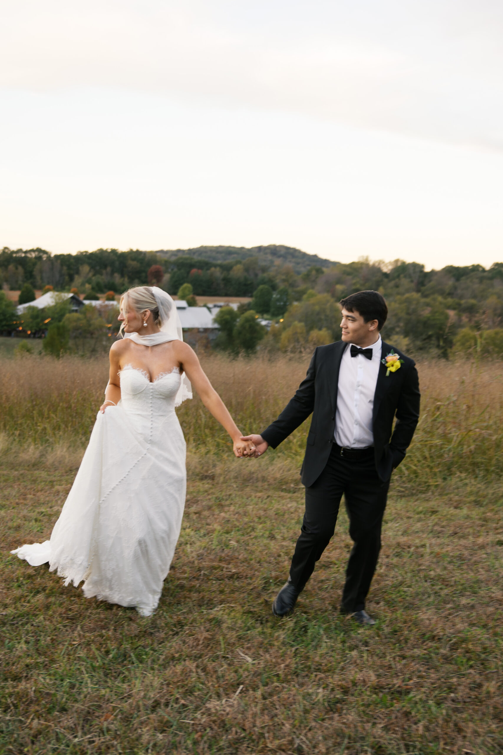 A couple who were just married hold hands in a field and are running looking behind them at mint springs farm