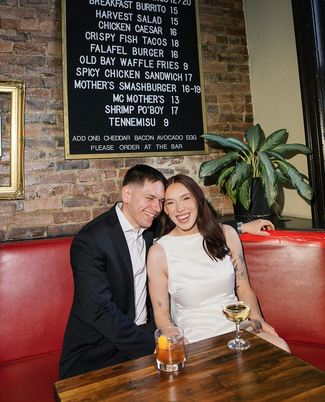 A couple holding onto each other sitting at a red bench laughing at a bar in nashville.