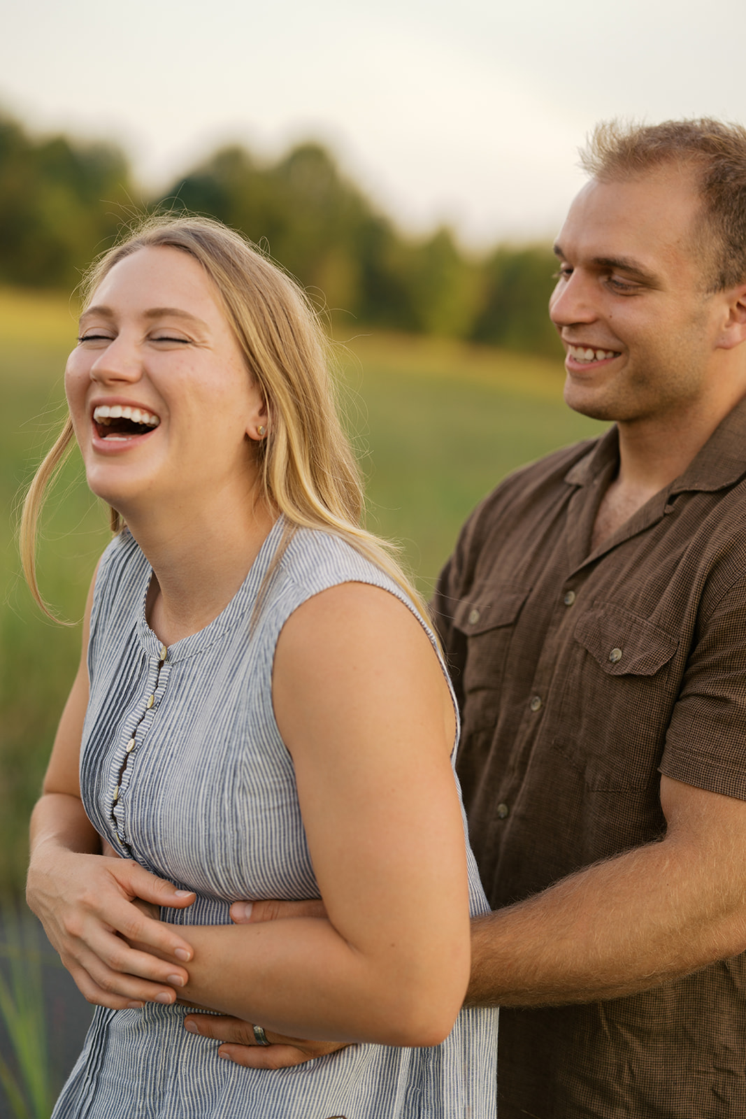 a couple laughing during their engagement session wearing a blue dress and brown button down shirt
