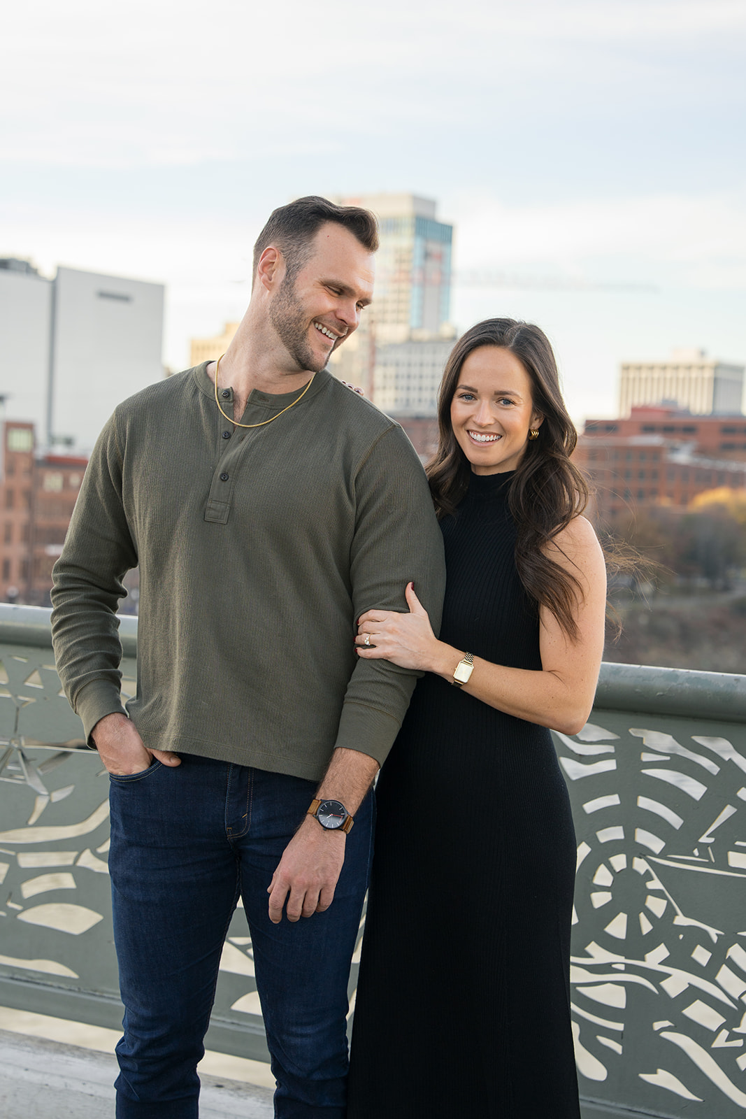 a woman wearing a black dress next to a man in a green shirt laughing during their nashville engagement session