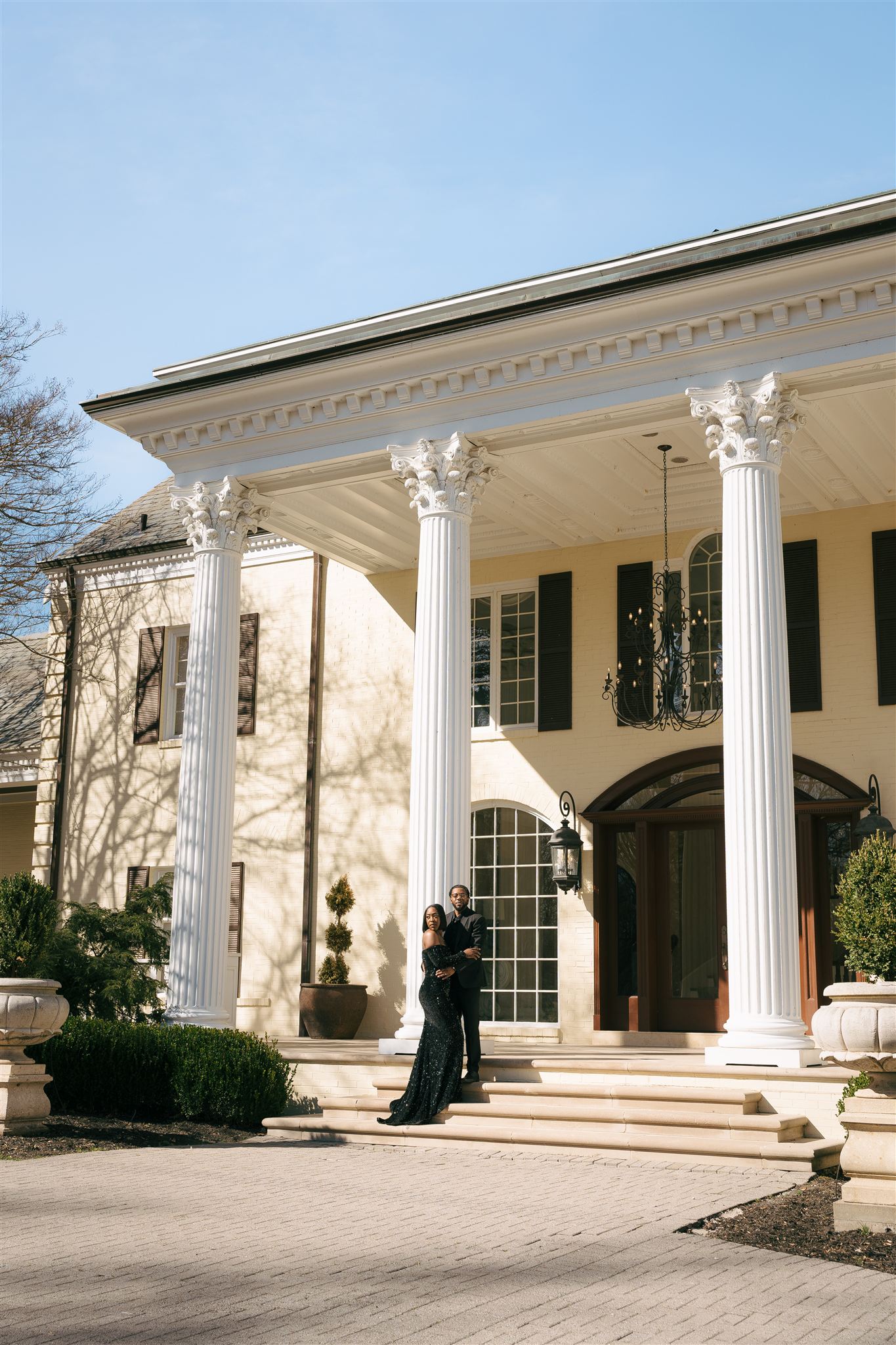 a couple out front of the estate at cherokee dock posing in a black dress and suit