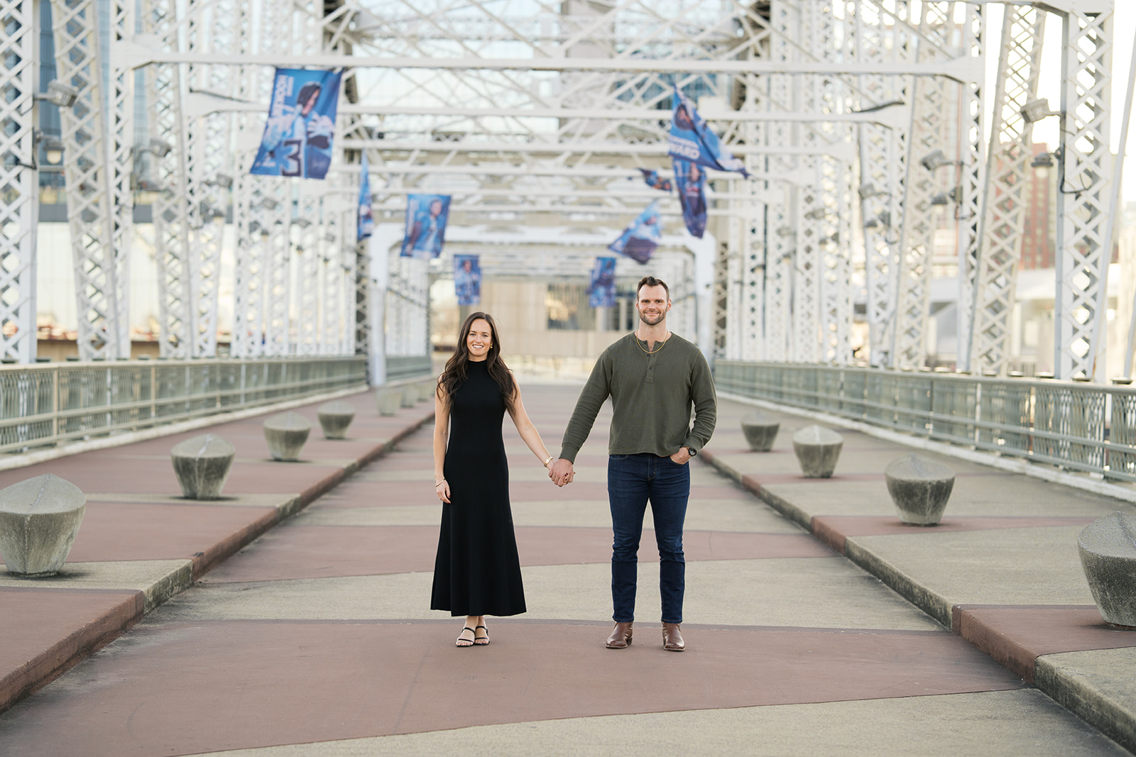 a couple holding hands looking at the camera at the pedestrian bridge in nashville, tennessee.