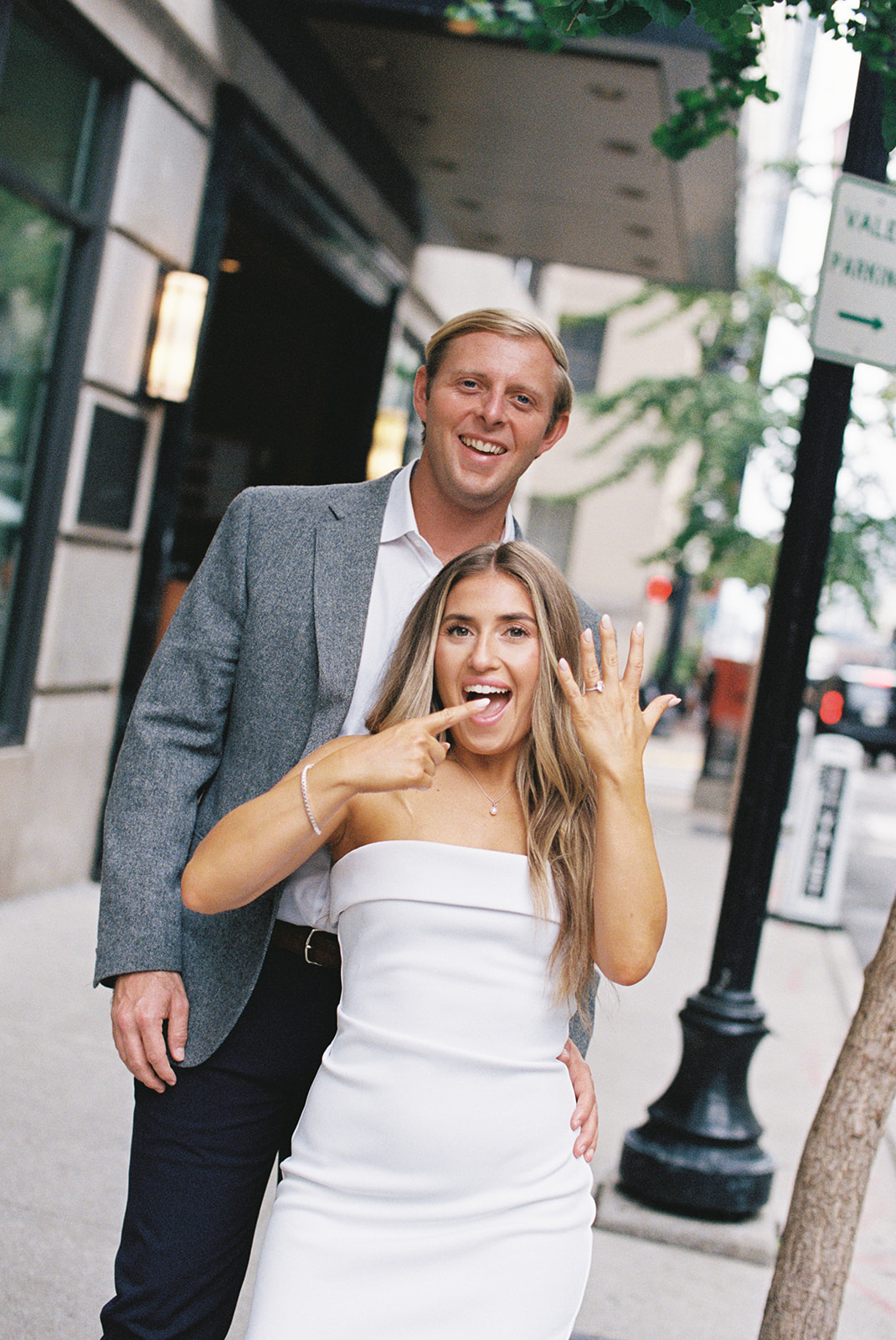 a woman wearing a white dress points to her engagement ring smiling after her nashville proposal