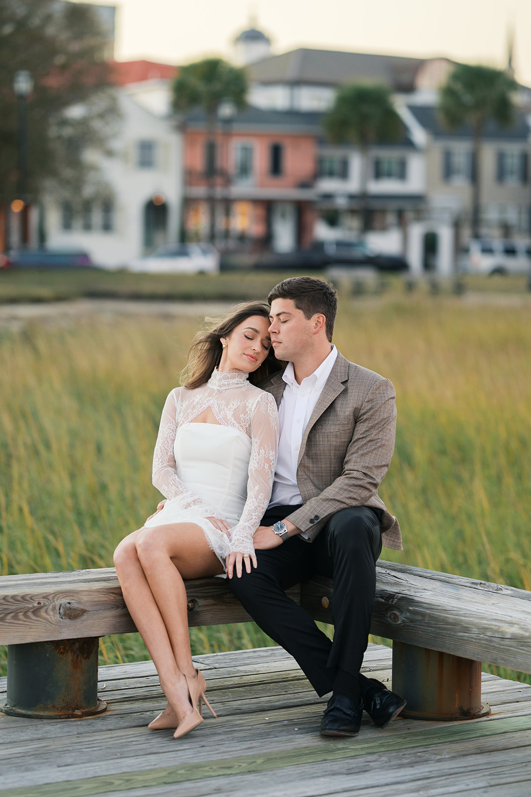 A couple sitting on a bench with the marsh in the background in charleston south carolina during their engagement session. photos by jaimee raneigh photography.