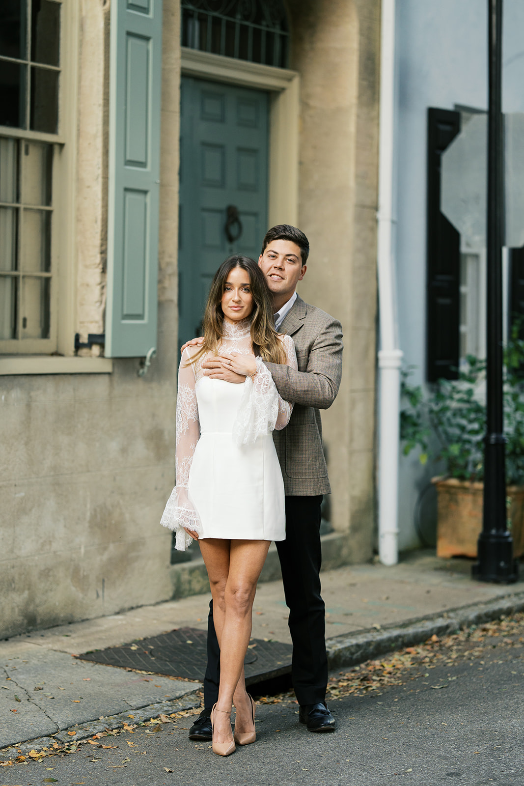 A couple looking at the camera in front of a blue historic home in charleston south carolina for their engagement photos.