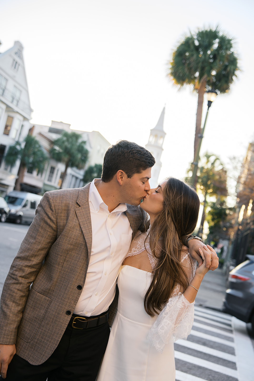 A couple walking on a cross walk during their engagement session in charleston with a church in the background