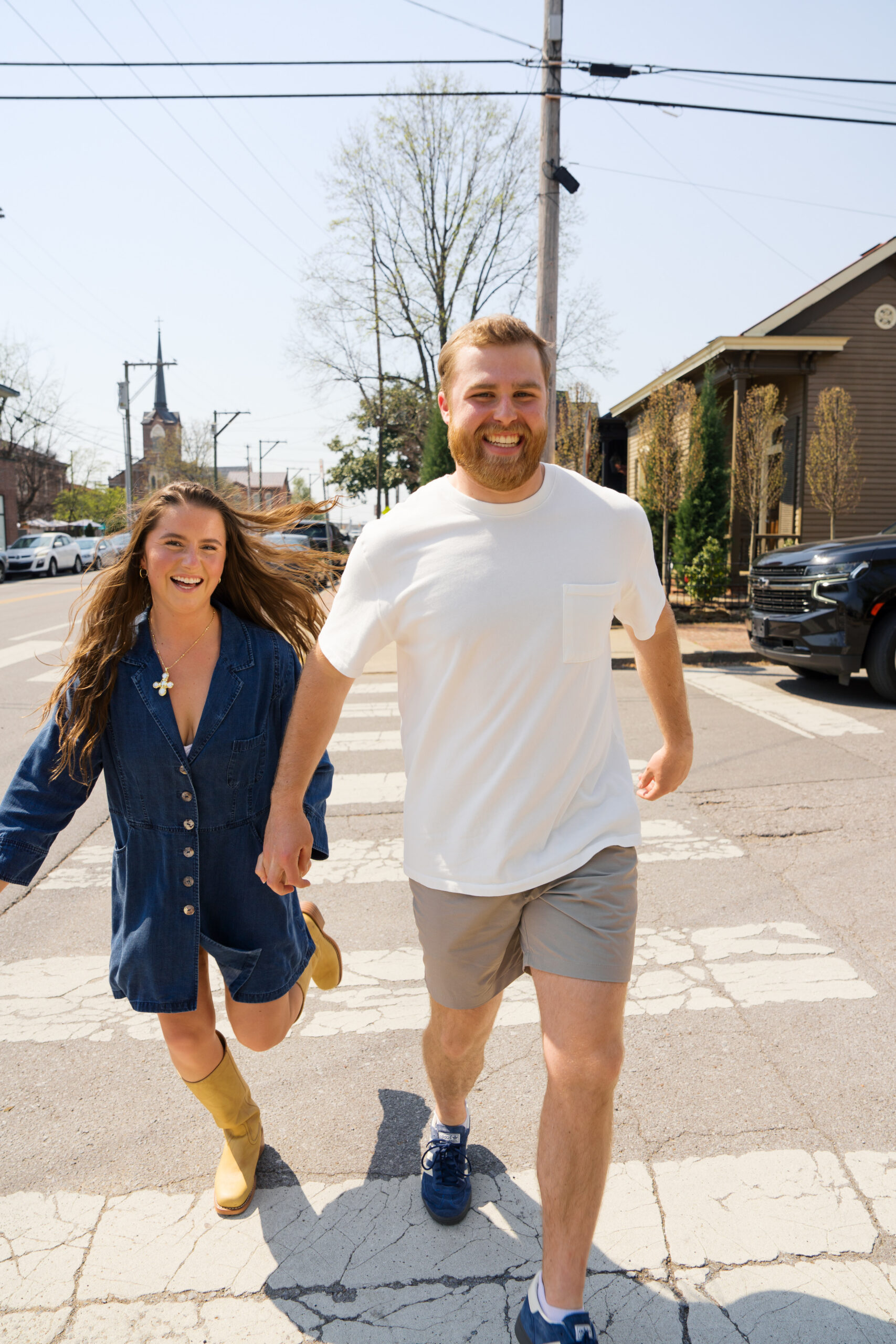 Couple laughs as they hold hands while running across a crosswalk.