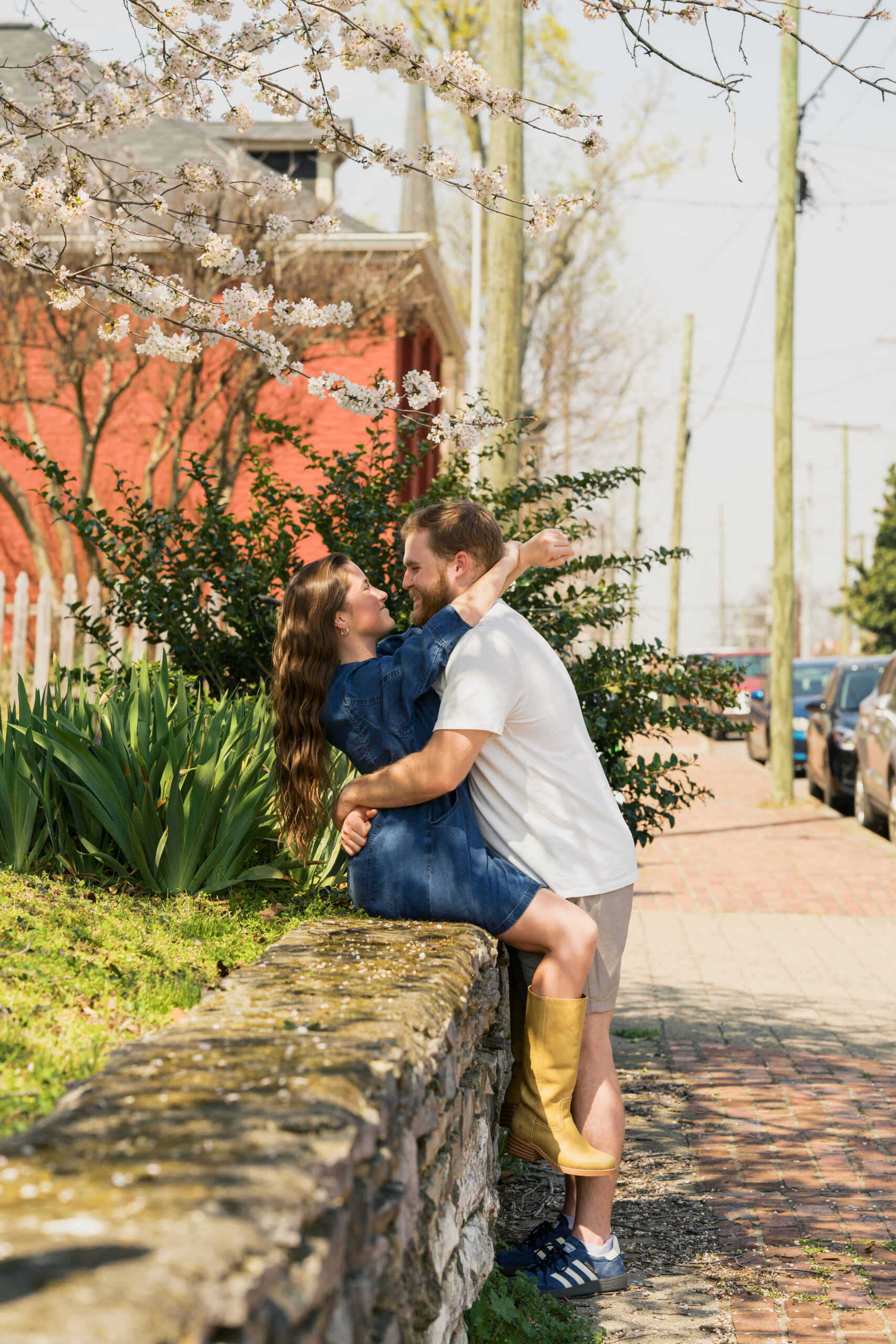 Woman sits on a brick wall while wrapping her arms around her fiances neck as he wraps his hands around her waist during their germantown engagement session in nashville tennessee.