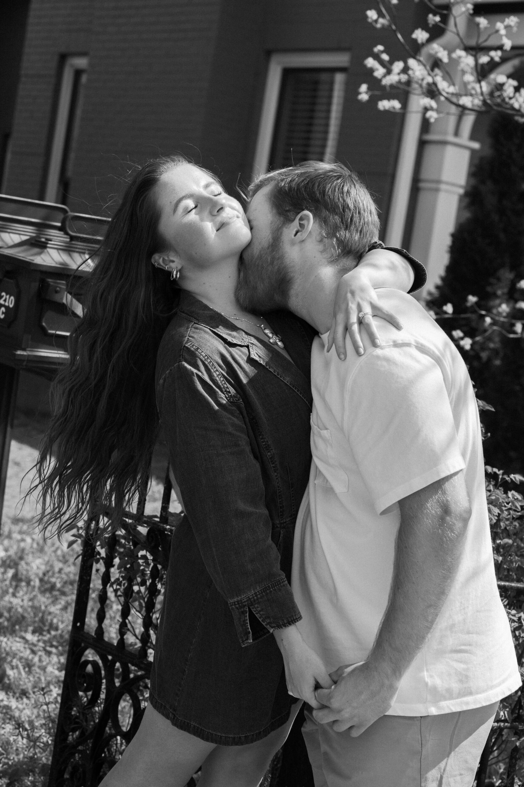Black and white photo of a man kissing his fiance's neck and she leans her head back.