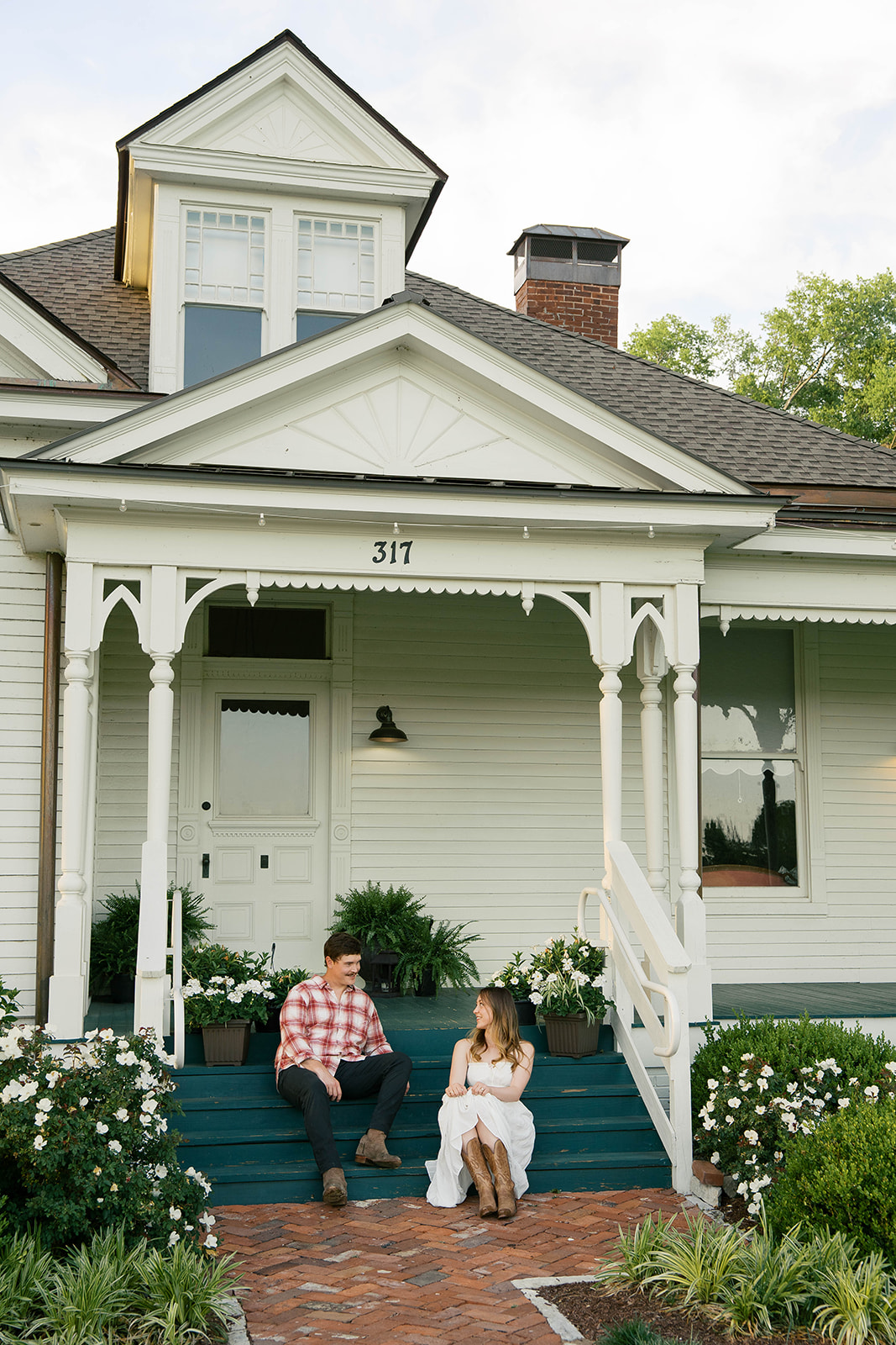 Couple laughs together as they sit on the front porch of a farm house. 