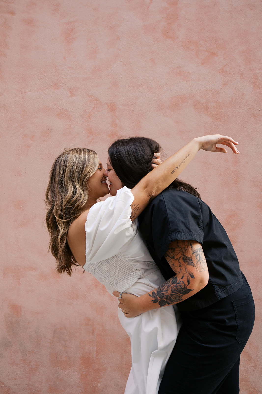 Two brides holding each others waist with a pink wall behind them during their savannah georgia engagement session.
