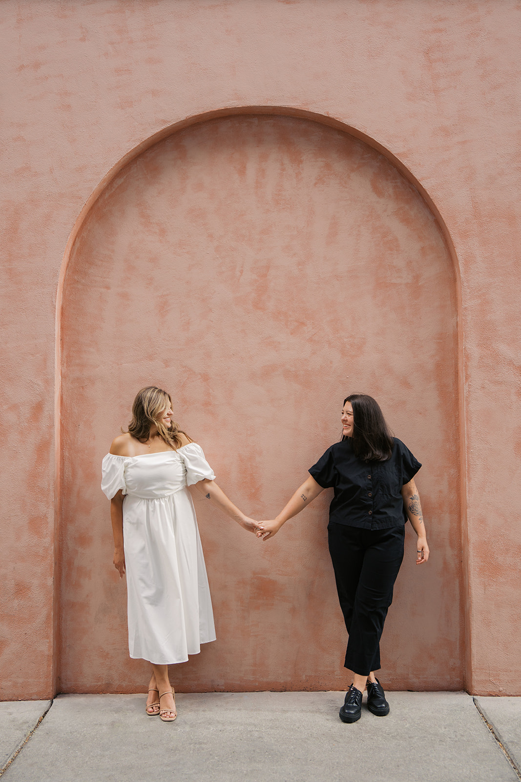 Two girls during their engagement session in savannah georgia photographed by jaimee raneigh photography in front of a pink stone arch.