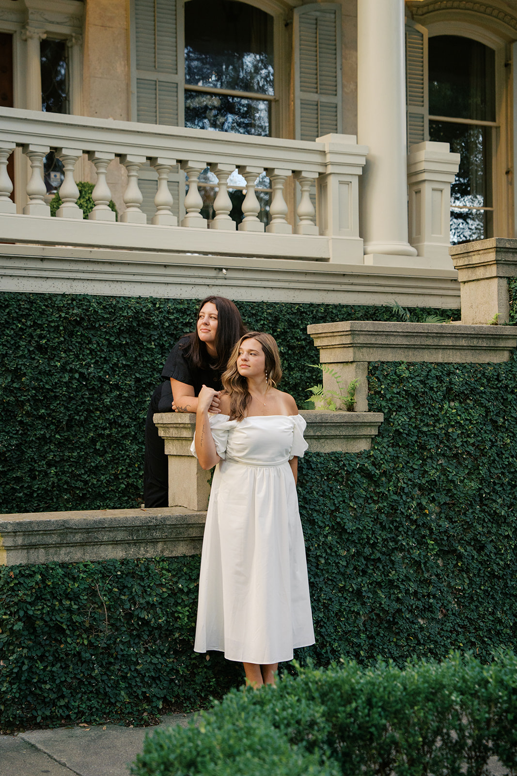 Two girls on an ivy lined stone house holding each other looking out. Photography by Jaimee Raneigh. 