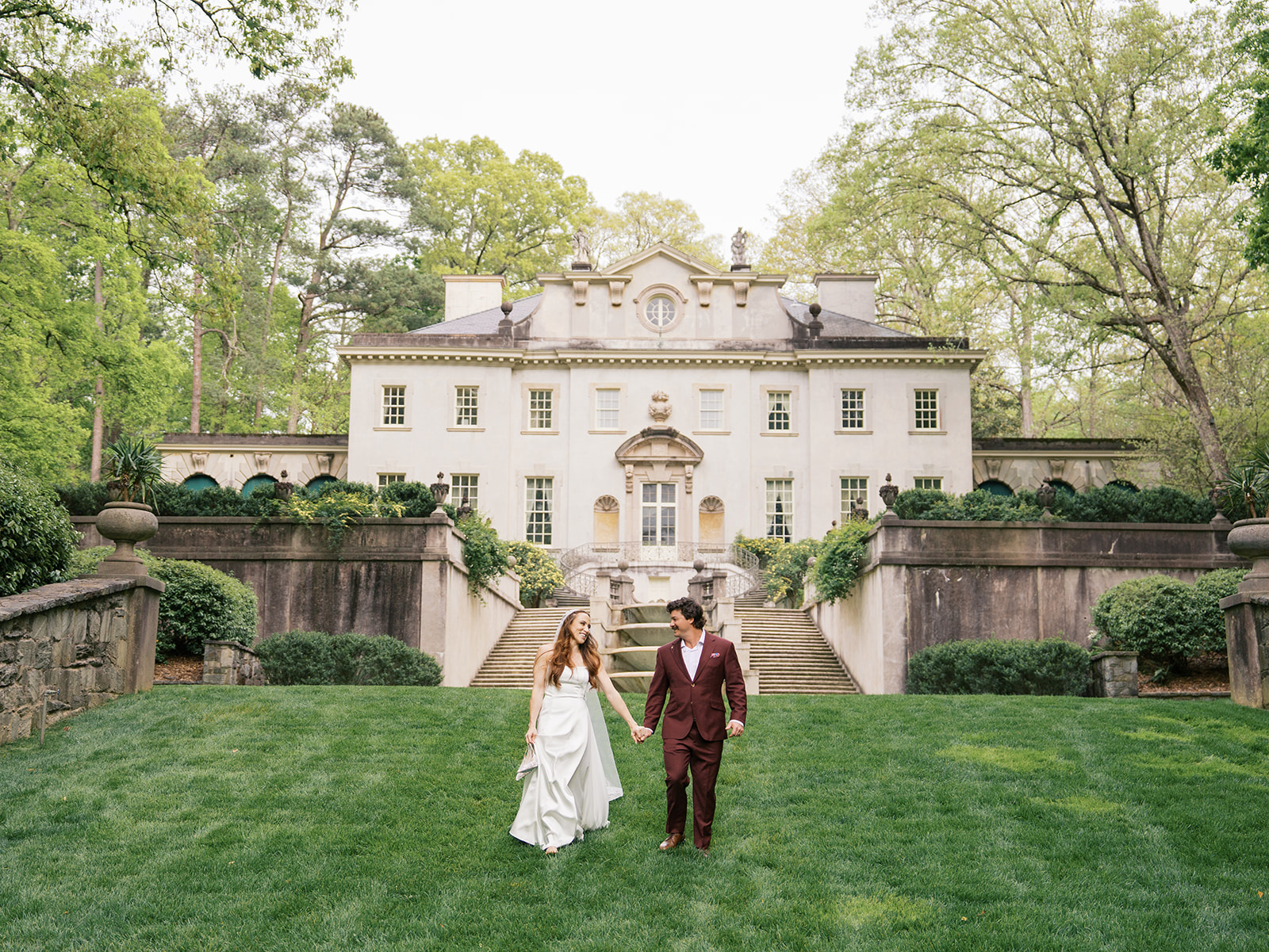 A couple in front of the lawn at the swan house holding hands walking towards the camera. Photos by Jaimee Raneigh