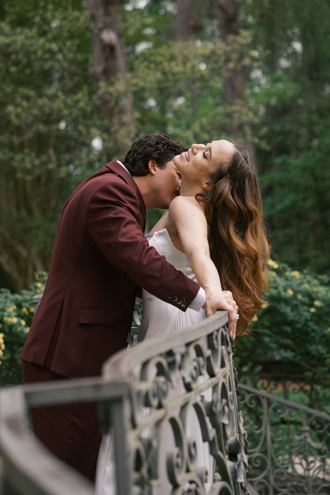 A groom wearing a red suit kissing the neck of his bride over a staircase at the Swan House in Atlanta Georgia on their wedding day.