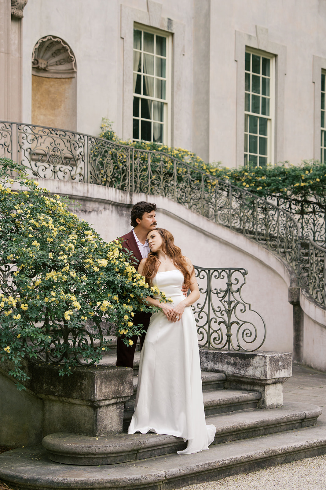 A couple on the stairs of the Swan House in Atlanta Georgia during their wedding day surrounded by a yellow flower bush.