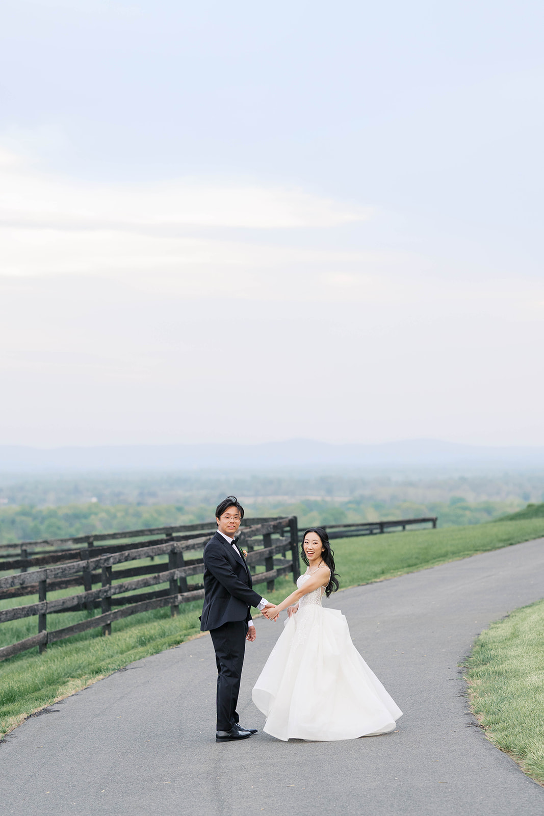 A couple holding hands looking back at the camera with a clear blue sky at the view at bluemont wedding venue in virginia. Photos by Jaimee Raneigh Photography.
