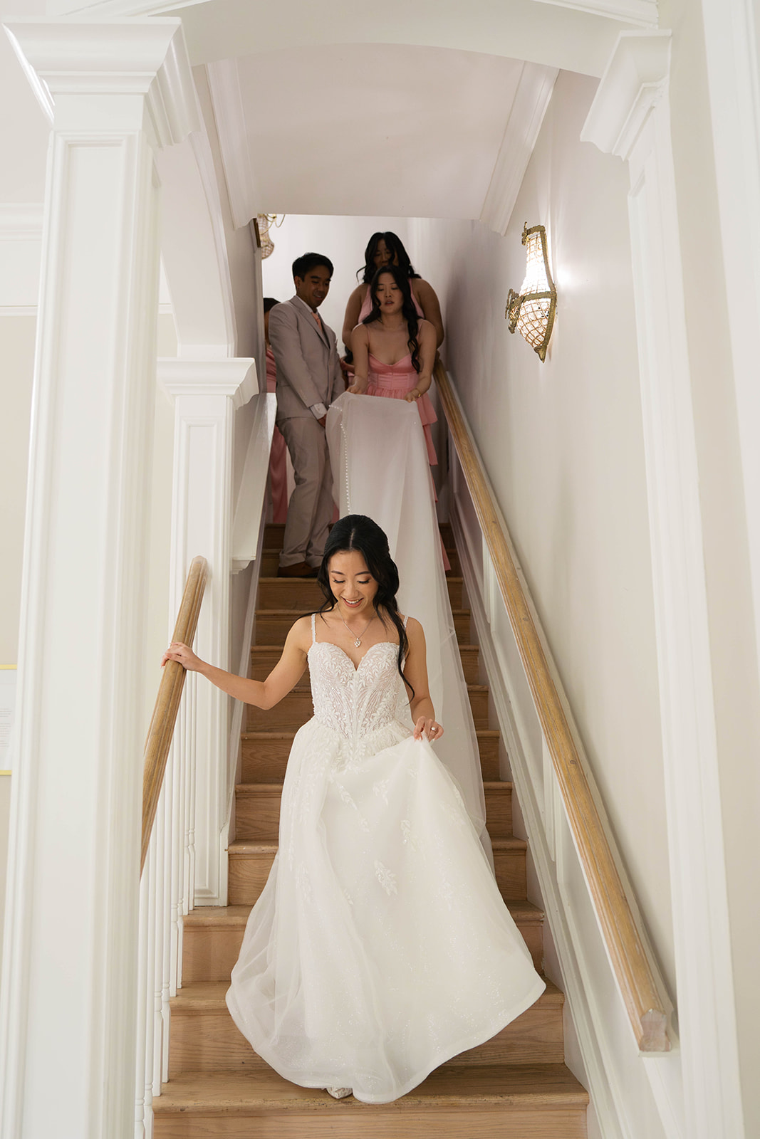 A bride walking down the stairs at the view at bluemont with her bridal party holding her dress as she walks. Photography by Jaimee Raneigh Photography.