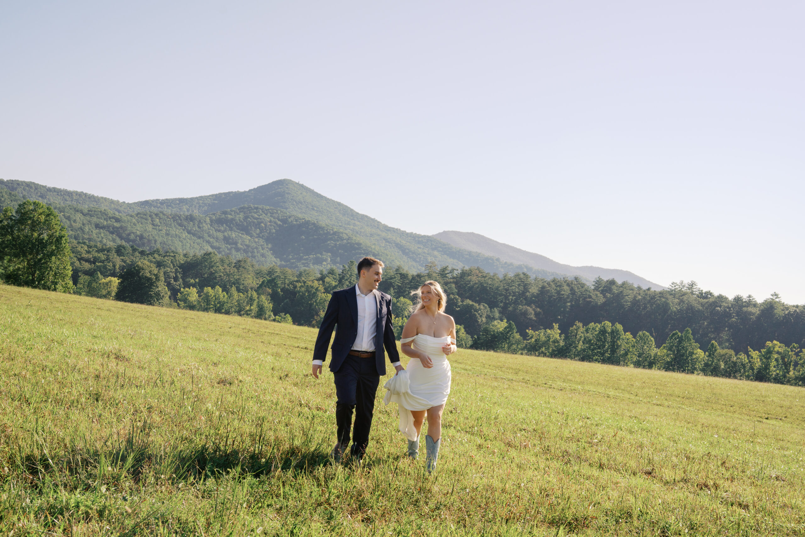 A couple holding hands running through a field during their elopement in the smoky mountains national park. Photography by Jaimee Raneigh Photography, a smoky mountain elopement photographer. 